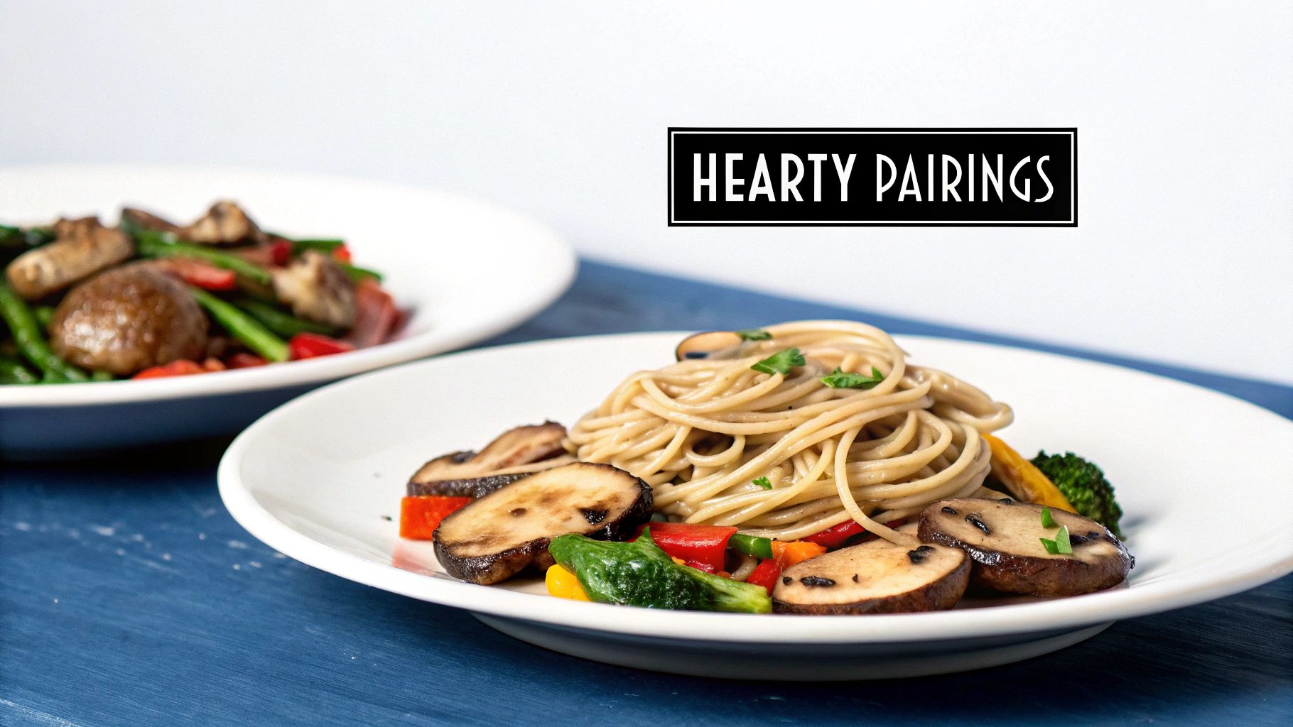 A plate of whole grain spaghetti with grilled mushrooms and colorful roasted vegetables on a blue table.