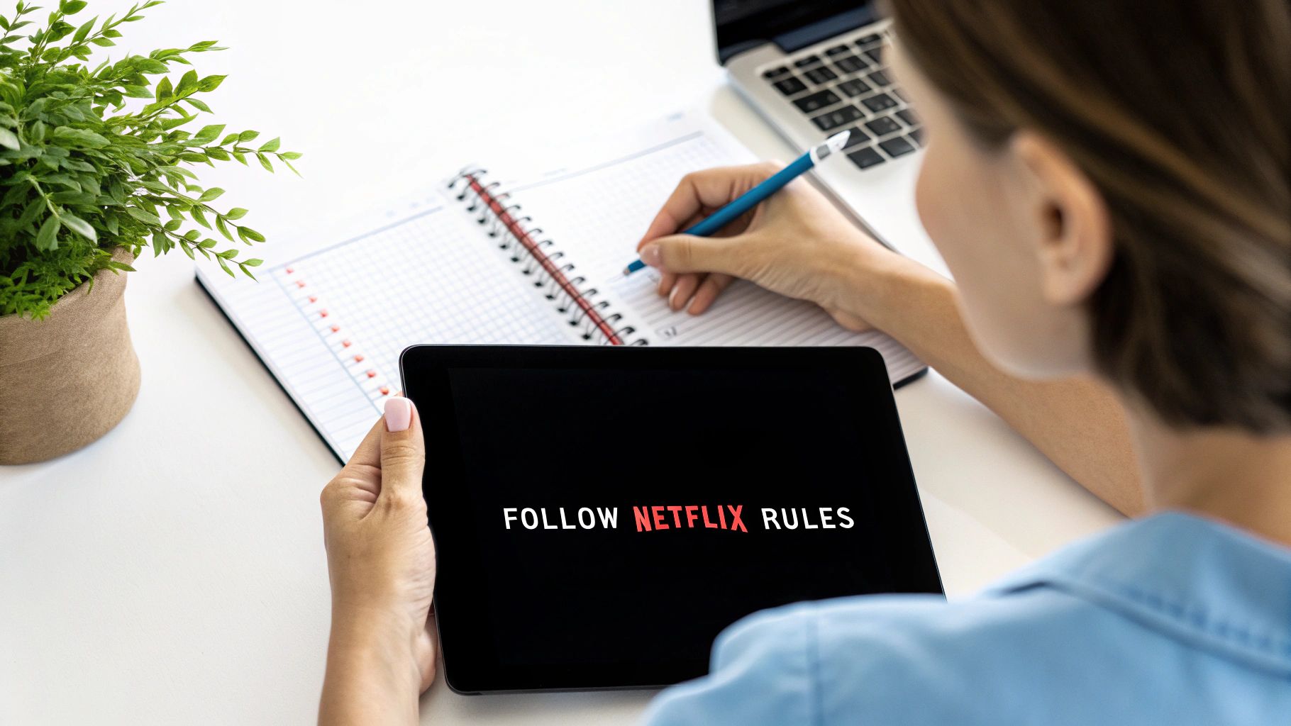 A person holds a tablet displaying 'FOLLOW NETFLIX RULES' while writing in a notebook.