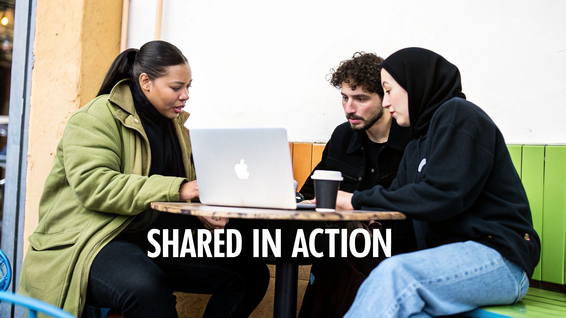 Three diverse young people collaborate on a laptop at an outdoor table with coffee.