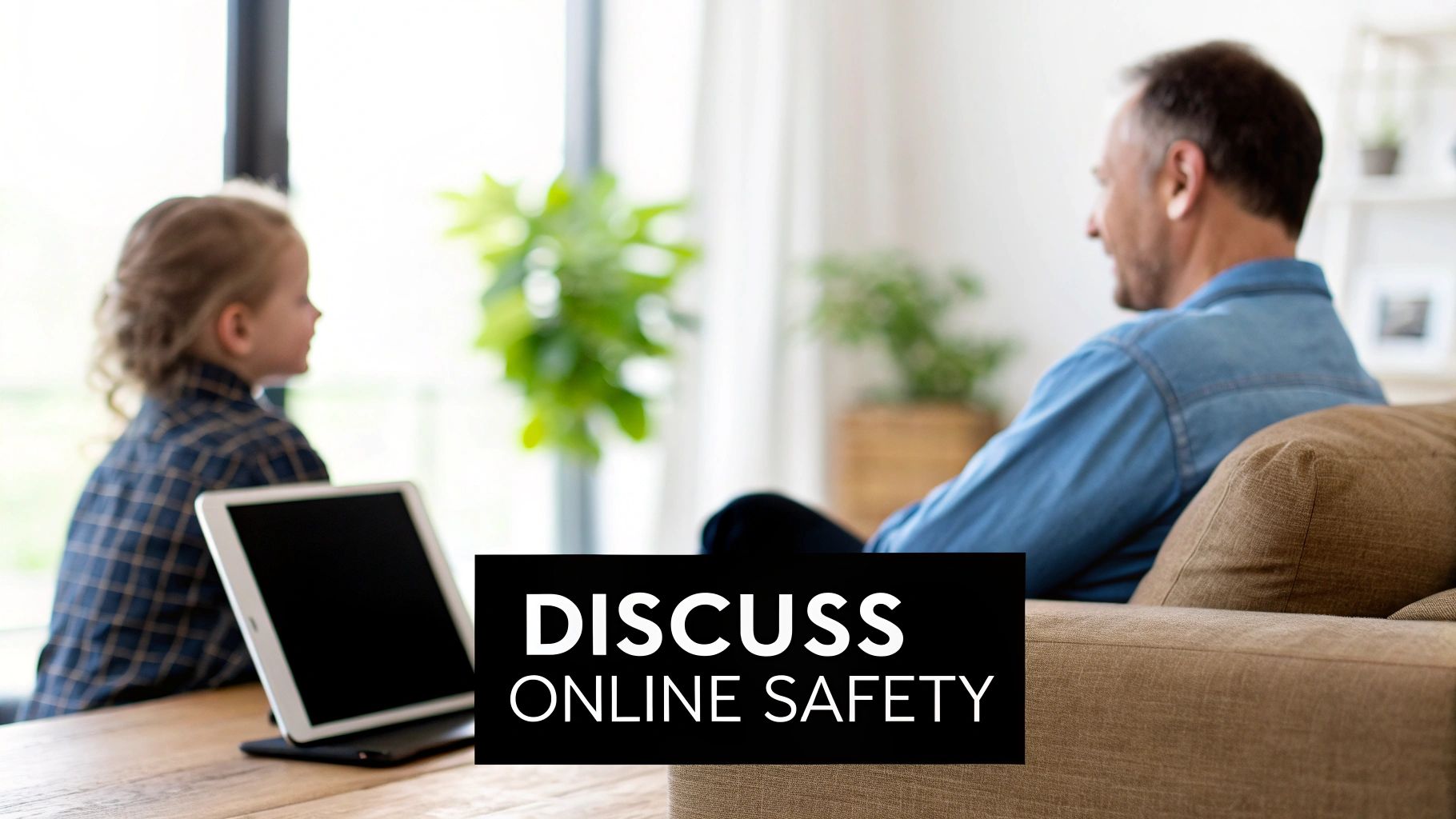 A parent and child are talking openly on a couch, with a tablet resting between them.