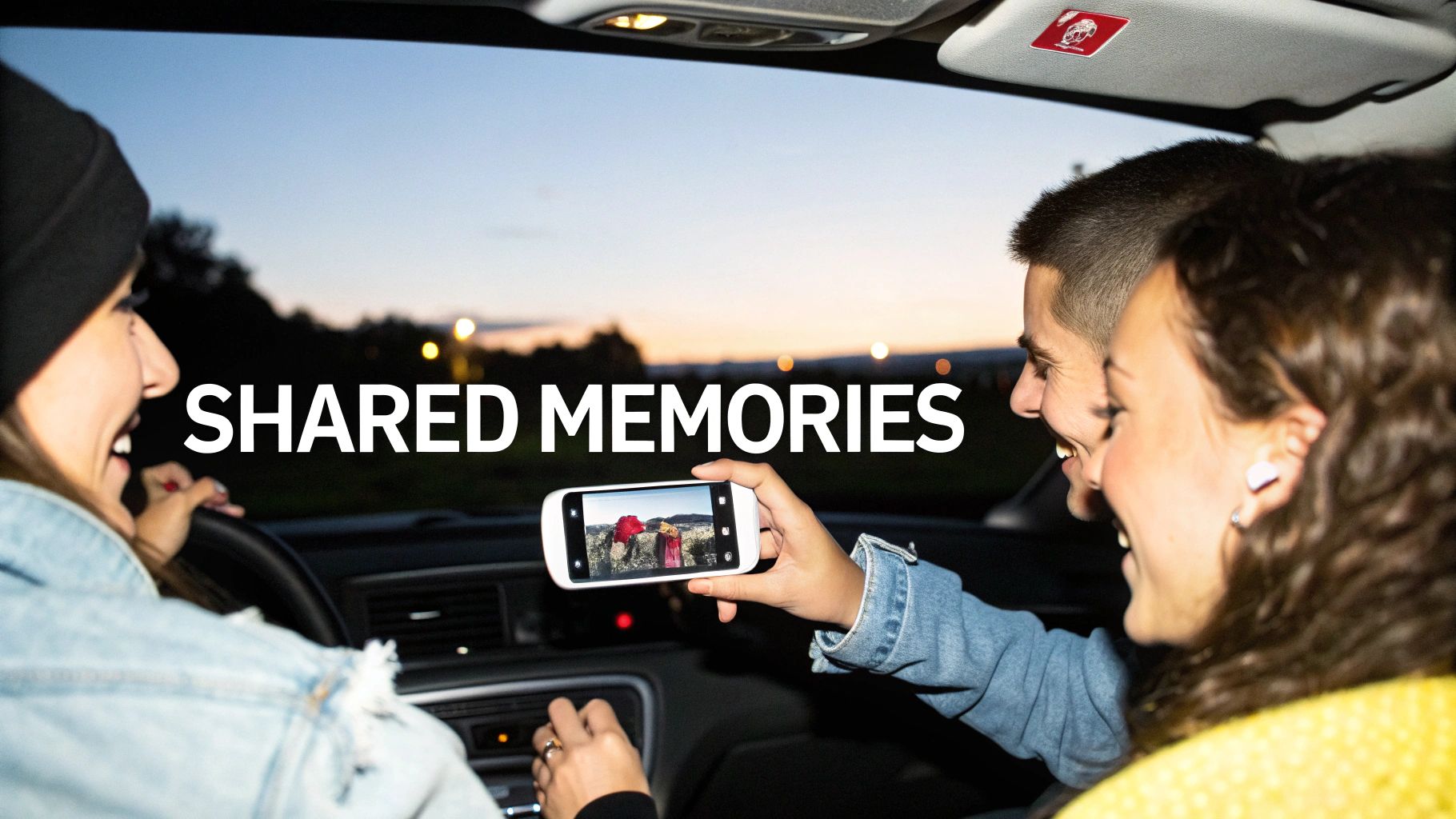 Three happy friends in a car sharing memories, looking at a photo on a smartphone.