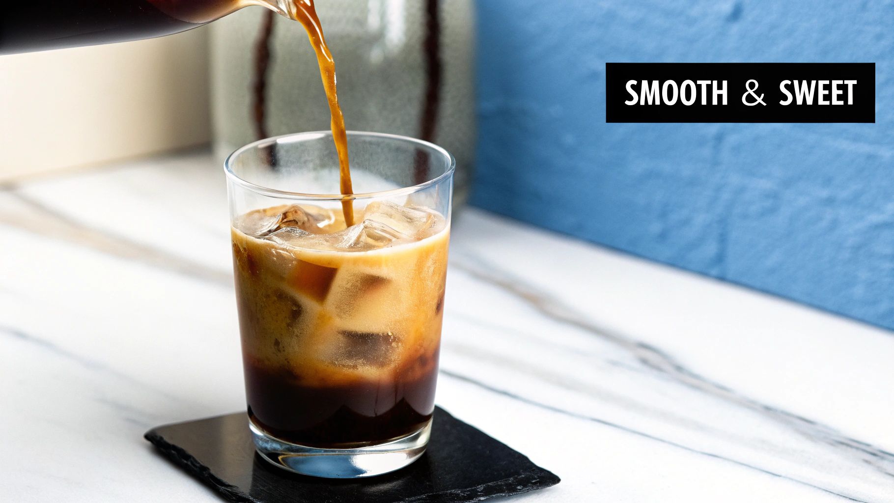 A close-up shot of cold brew coffee being poured from a glass pitcher into a glass filled with ice cubes, highlighting its smooth texture.