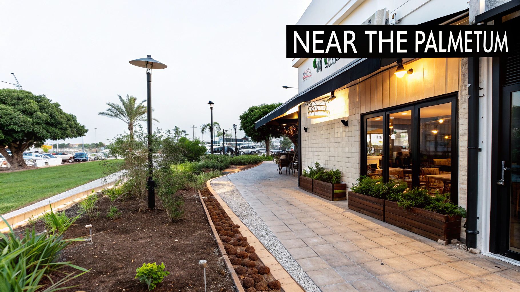 Exterior view of a modern cafe with outdoor seating, a paved path, and green landscaping.