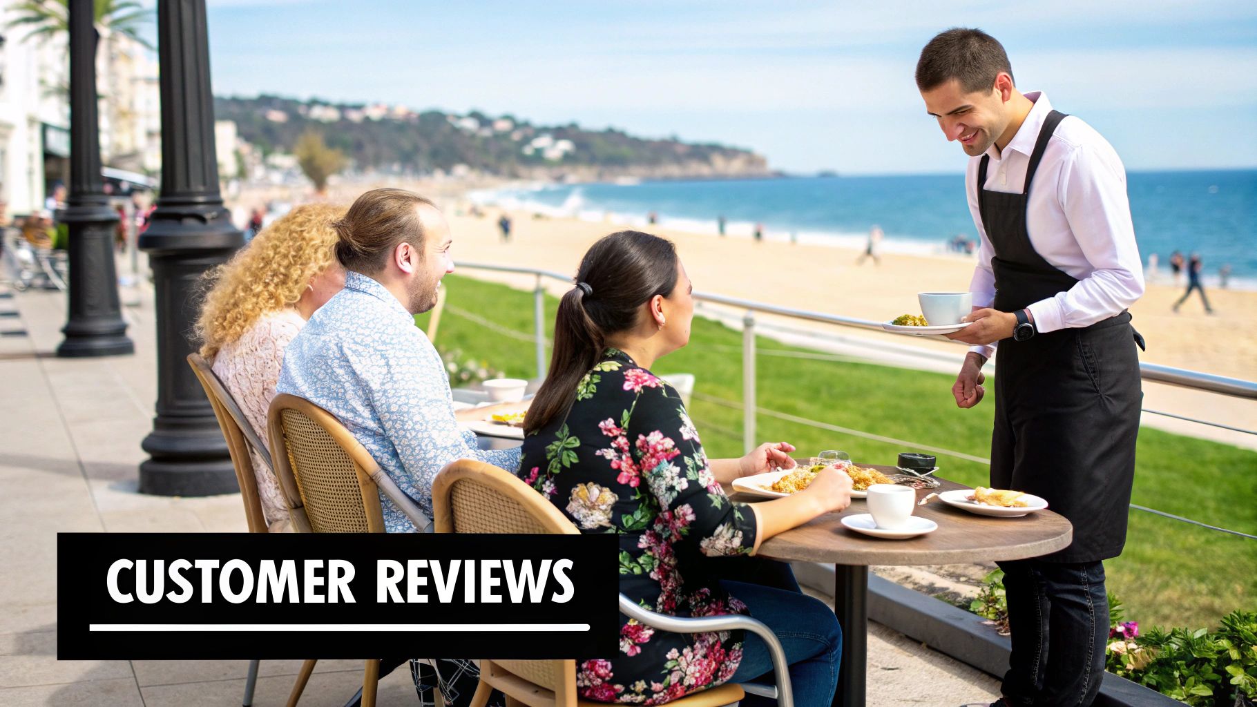 Smiling waiter serving customers at a vibrant outdoor cafe overlooking the beach and ocean.