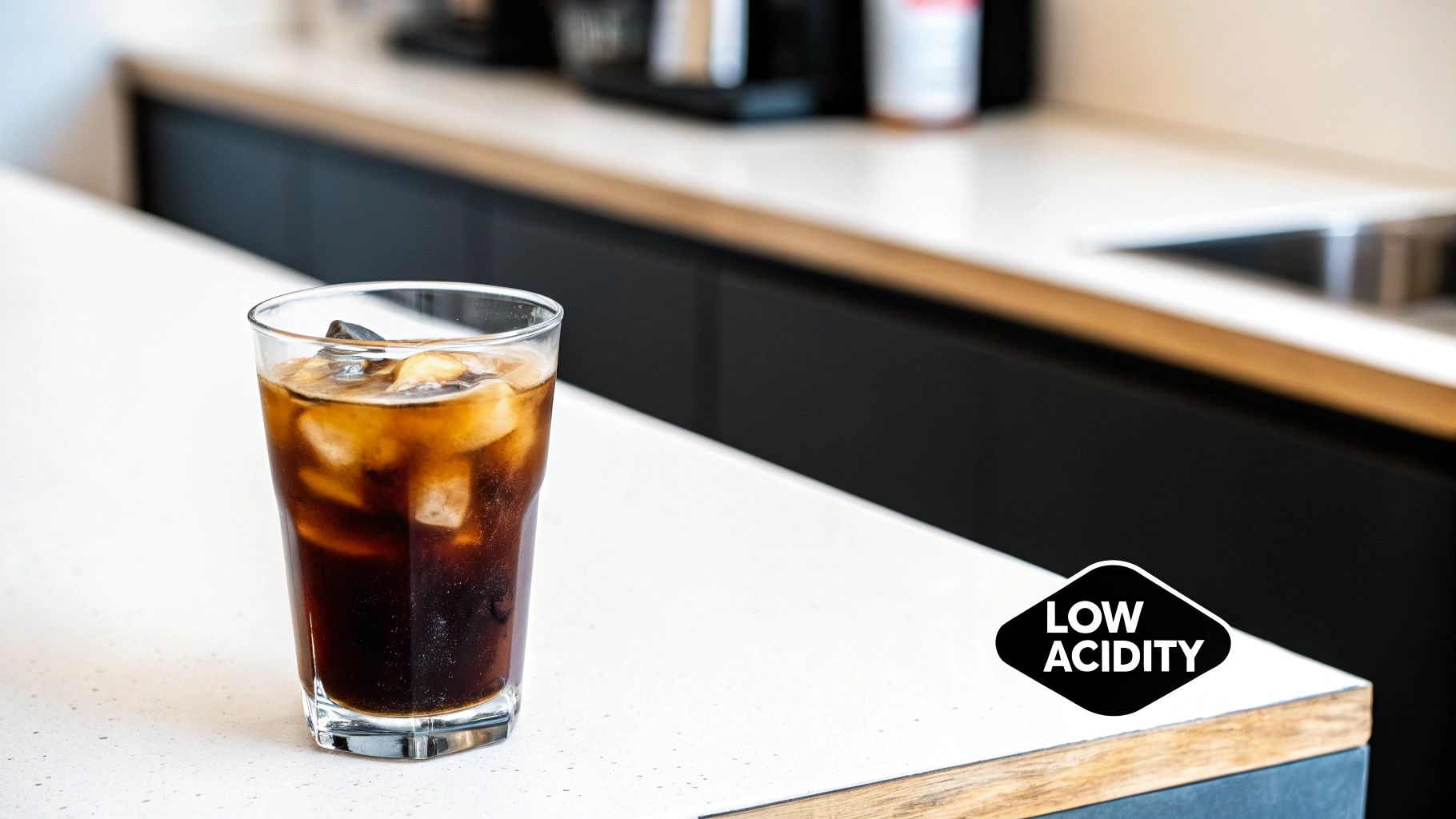 A glass of cold brew coffee with ice cubes and a metal straw, sitting on a wooden surface next to coffee beans.