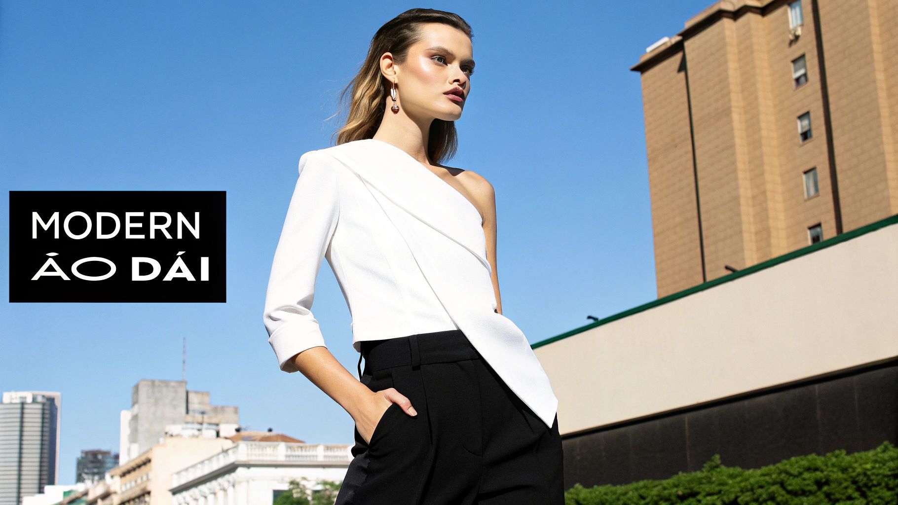 A stylish woman models a modern white one-shoulder top and black pants under a clear blue sky.