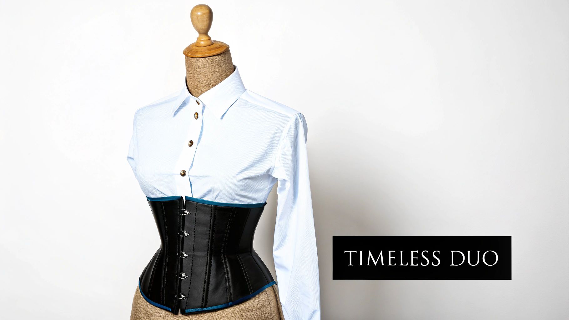 A mannequin wears a white button-up shirt and a black underbust corset with blue trim.