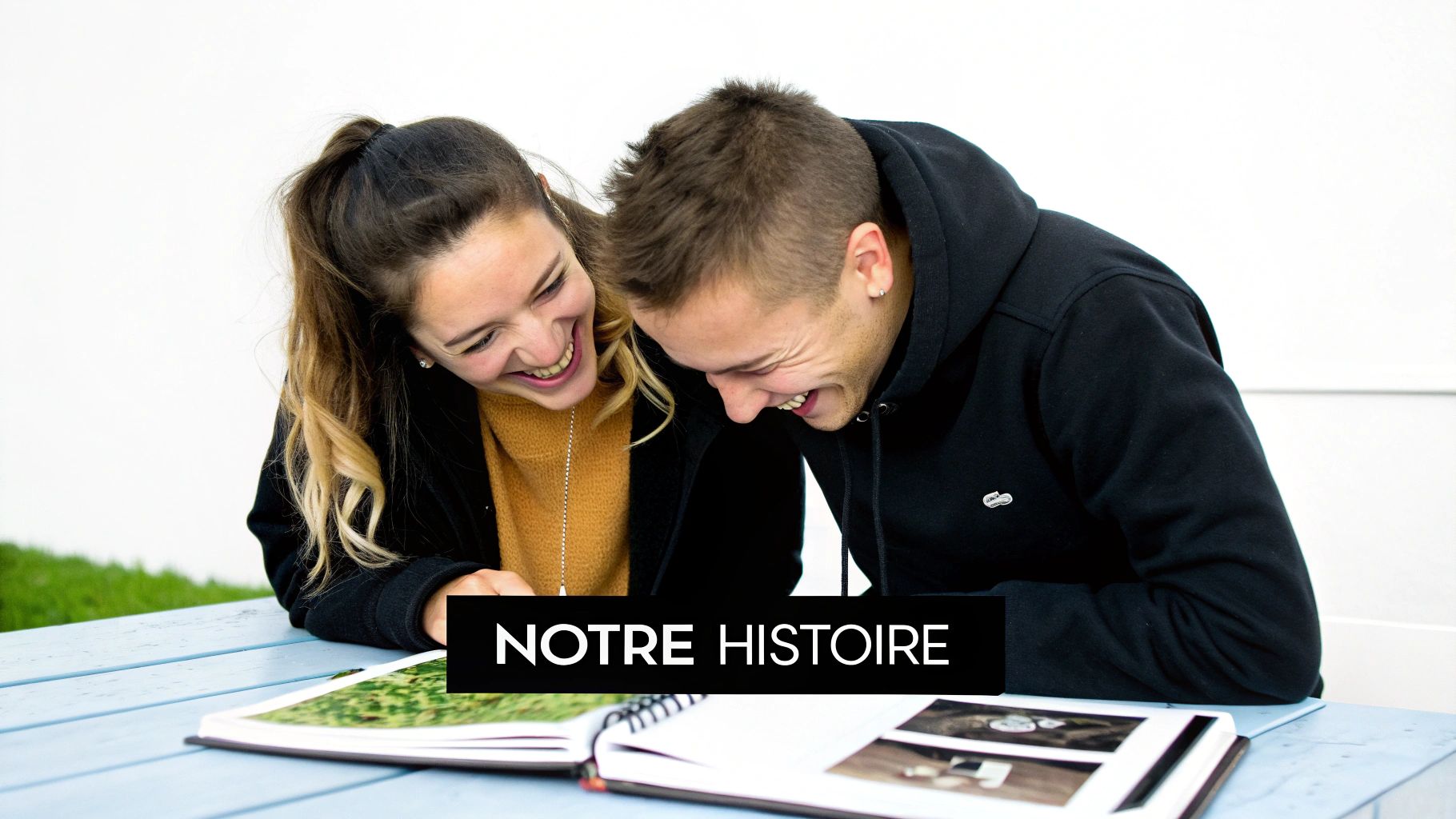 Un couple heureux et rieur regarde un livre photo sur une table, avec le texte "NOTRE HISTOIRE".