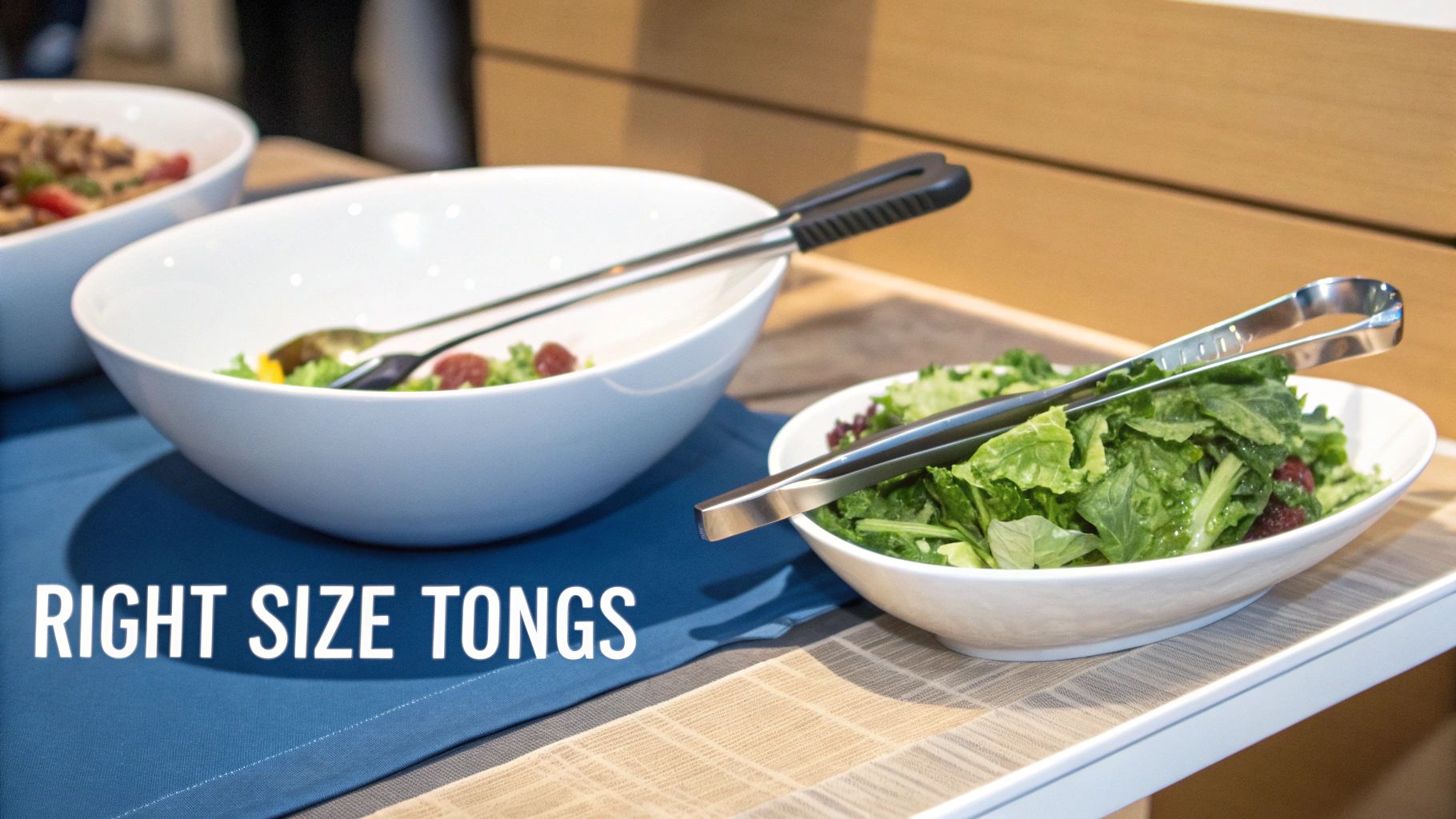A buffet setup features two white bowls of fresh salad, each with a pair of serving tongs.