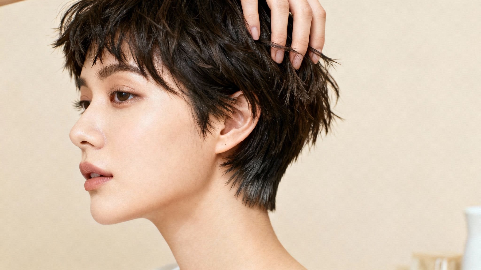 Close-up of a person running a hand through their short, dark, textured hair.