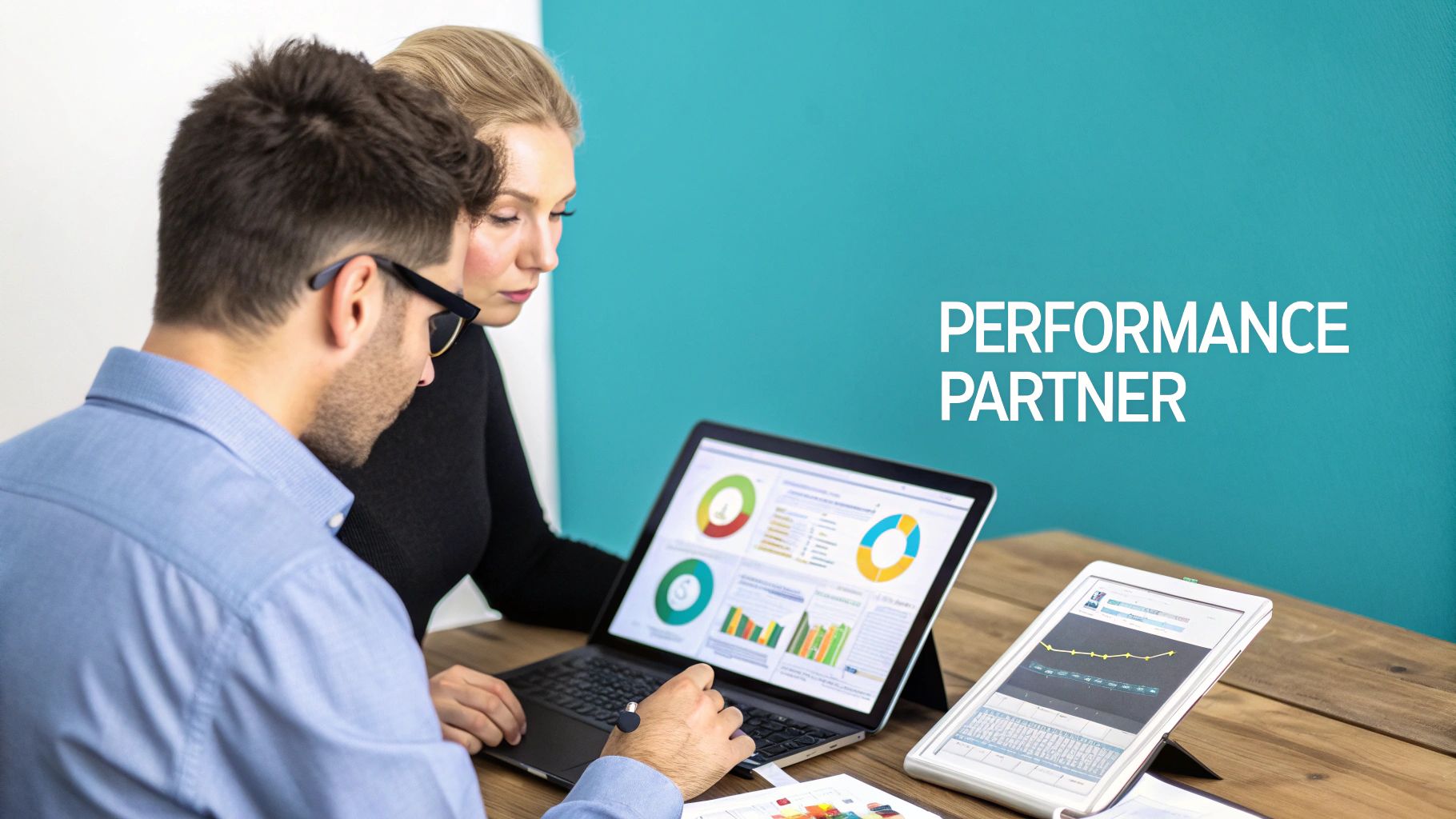Man and woman discussing data and charts on a laptop, with 'PERFORMANCE PARTNER' on the wall.
