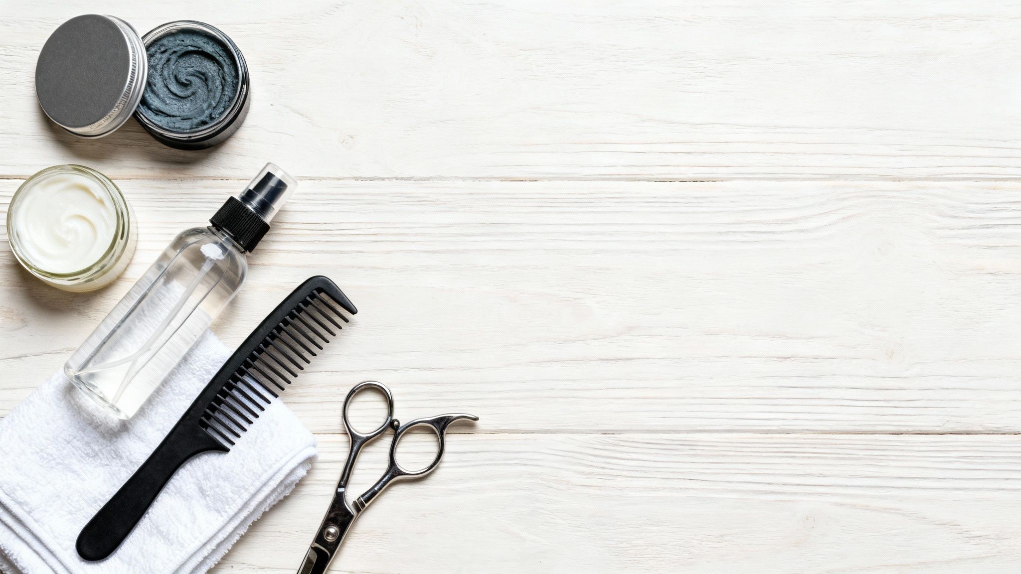 Flat lay of hairdressing tools and products including comb, scissors, and hair creams on a white wooden background.