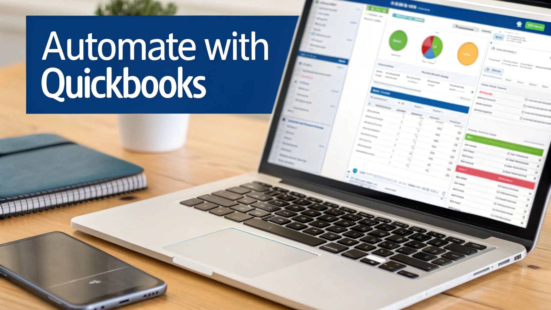 A laptop on a wooden desk showing QuickBooks software, with a notebook and smartphone.