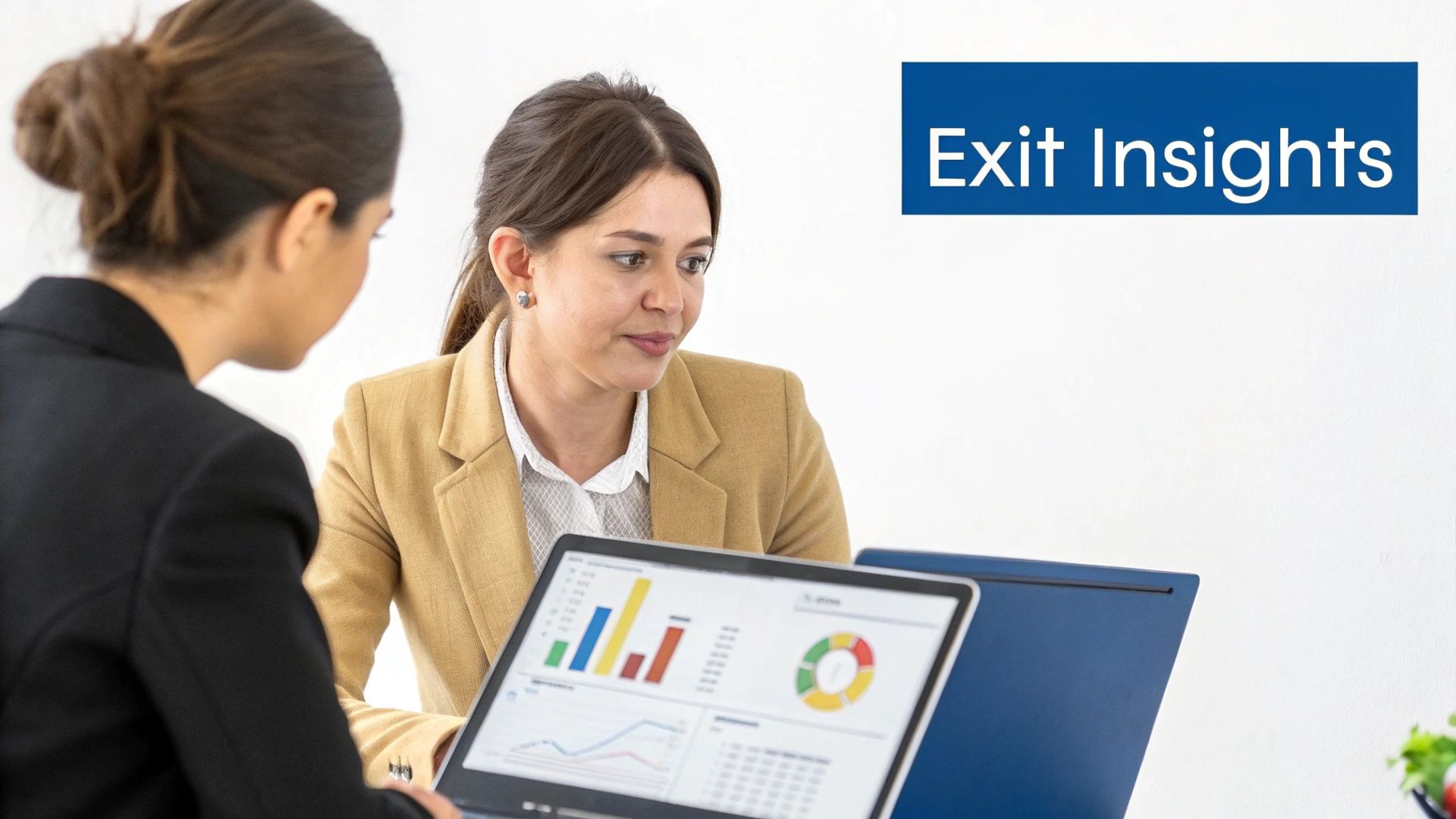Two businesswomen analyze data on a laptop displaying charts and graphs during a meeting.