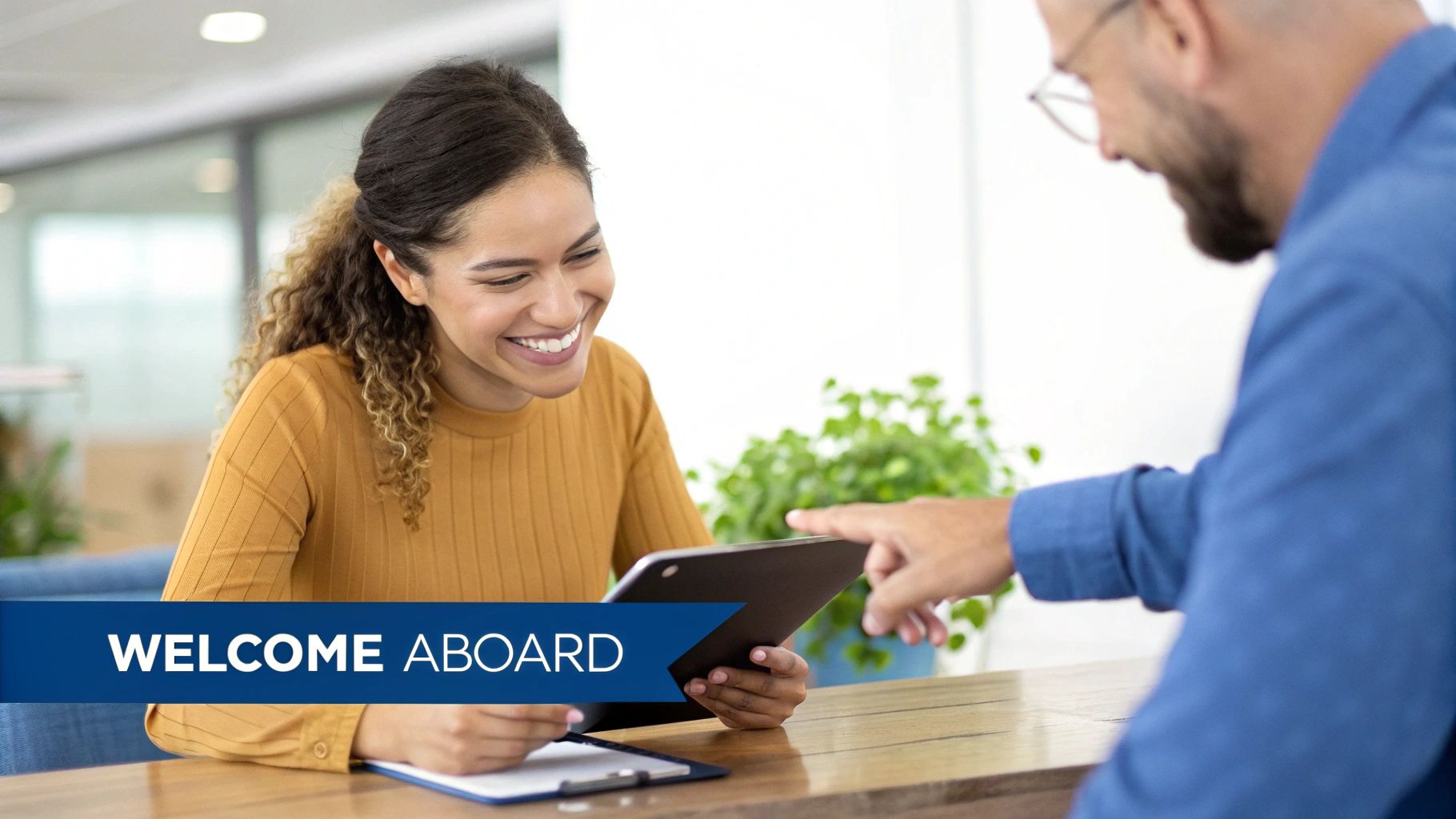 Smiling woman reviews documents on a tablet with a colleague during a welcome aboard session.