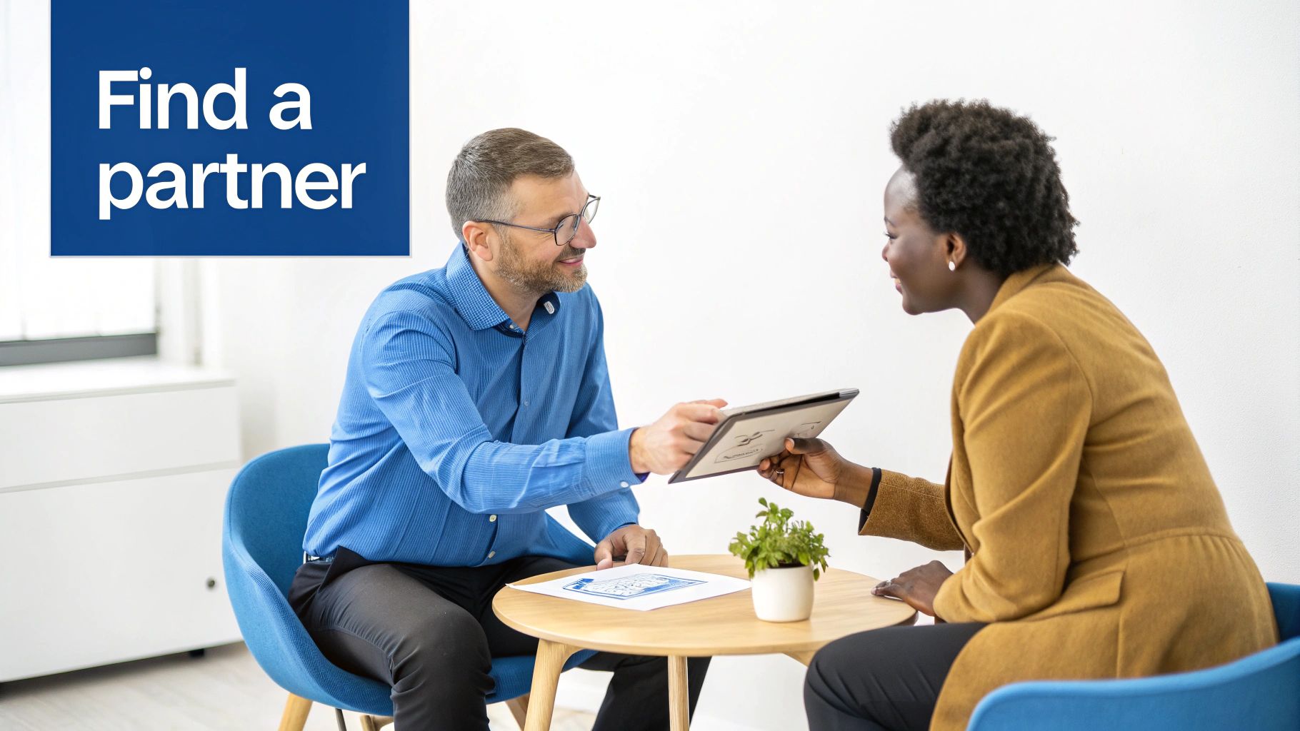 Two business partners collaborate, with a man handing a tablet to a smiling woman during a meeting.