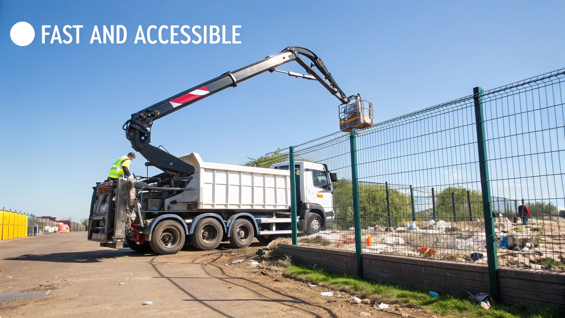A worker in a high-vis vest operates a grabber lorry lifting a bucket over a fence, clearing waste.