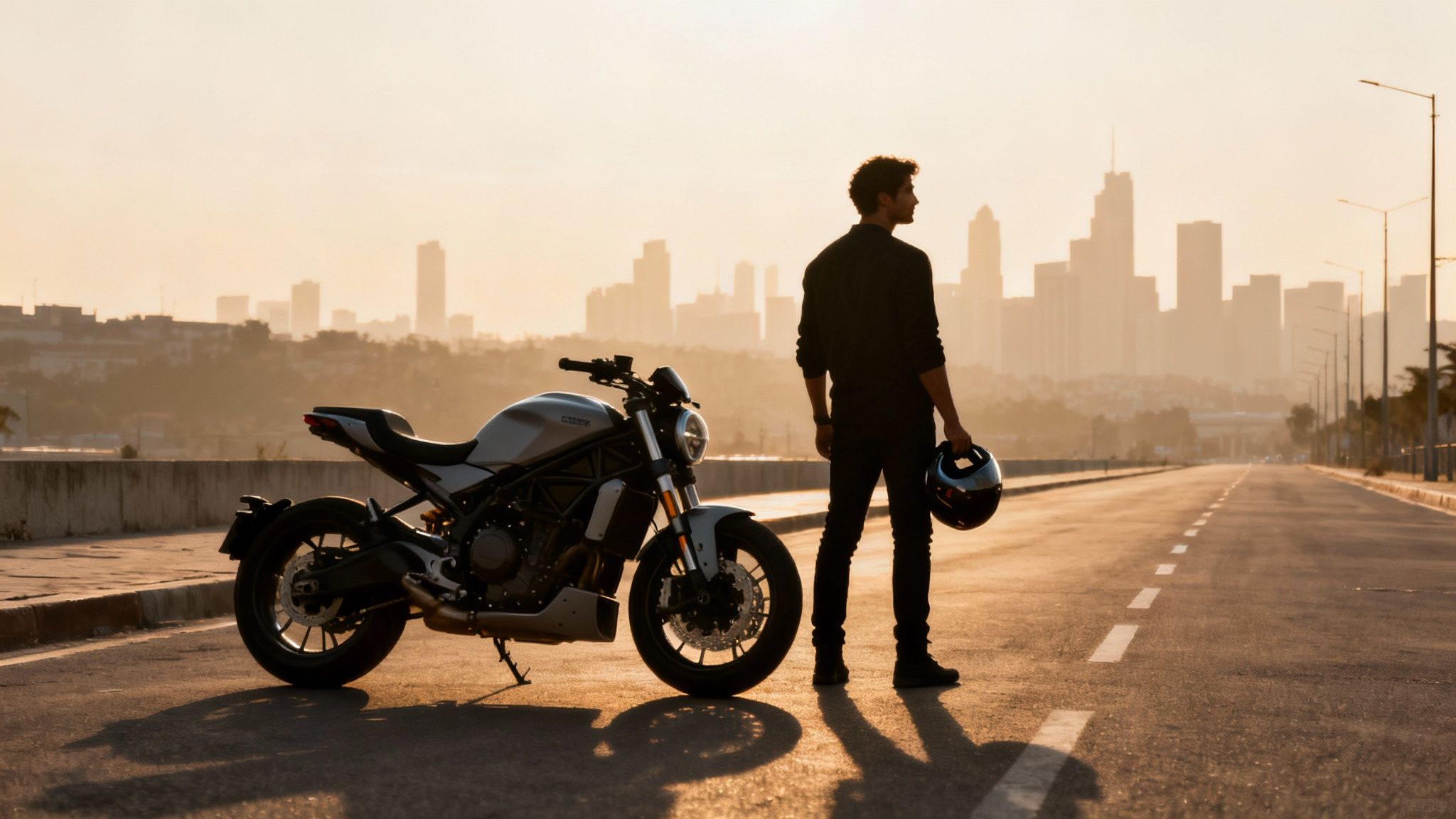 גבר עומד עם קסדה ליד אופנוע על כביש רחב בשקיעה, עם עיר מרוחקת ברקע.