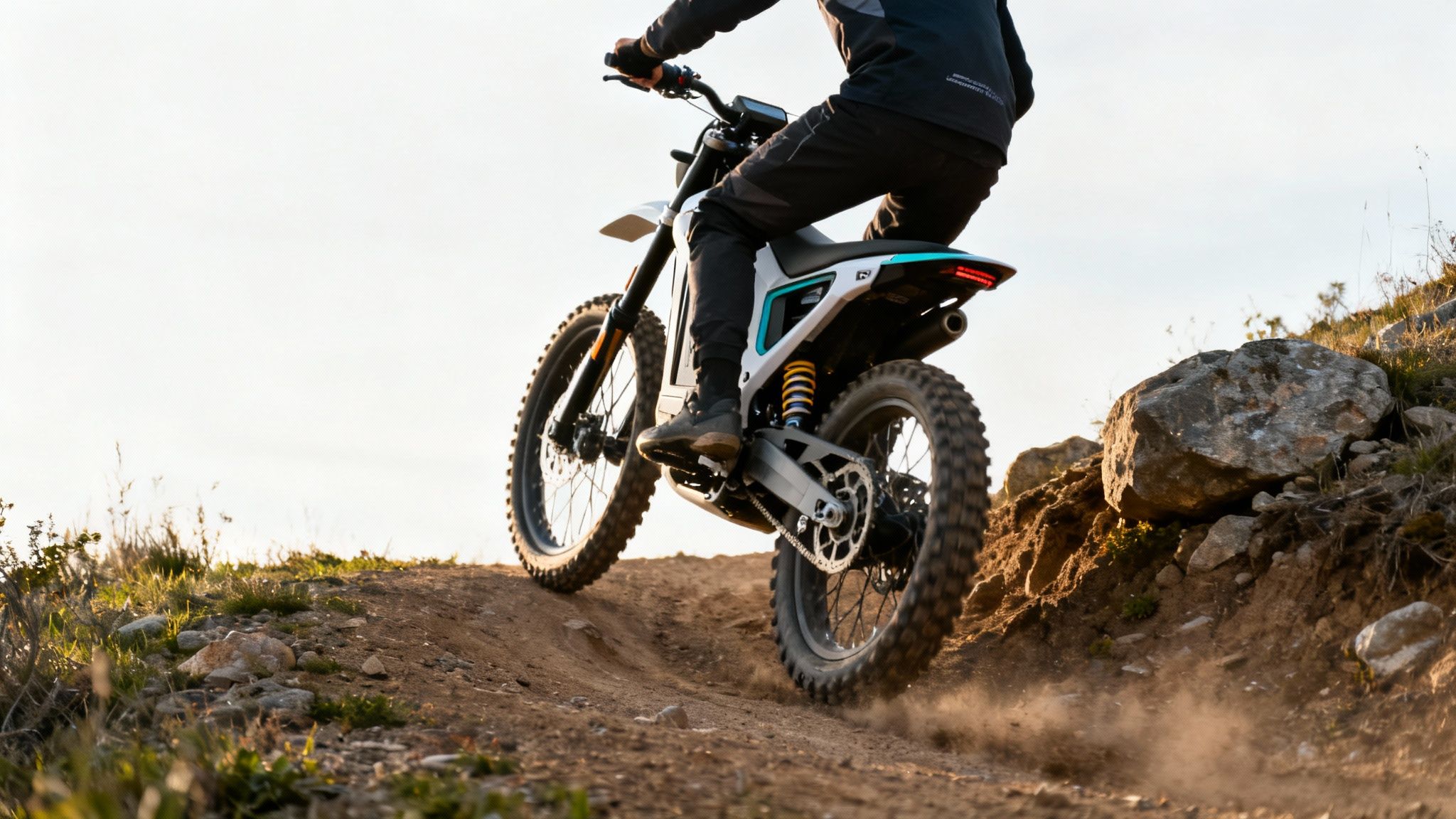 רוכב על אופנוע שטח חשמלי לבן בשביל עפר, כשהוא מעלה ענן אבק בשקיעה.