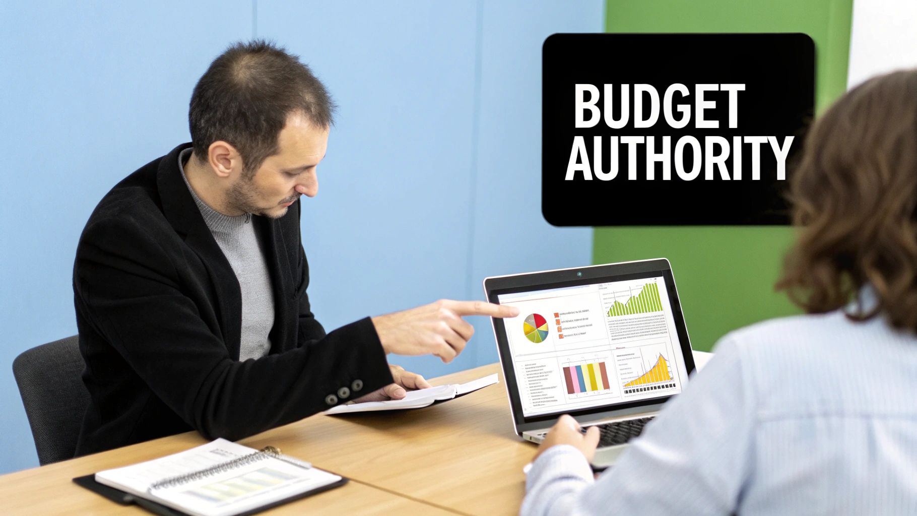 Two colleagues discuss financial data and charts on a laptop screen during a 'Budget Authority' meeting.