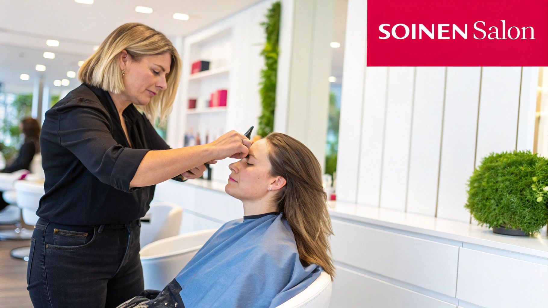 Une coiffeuse blonde et souriante s'occupe des sourcils d'une cliente dans un salon de coiffure moderne et lumineux.