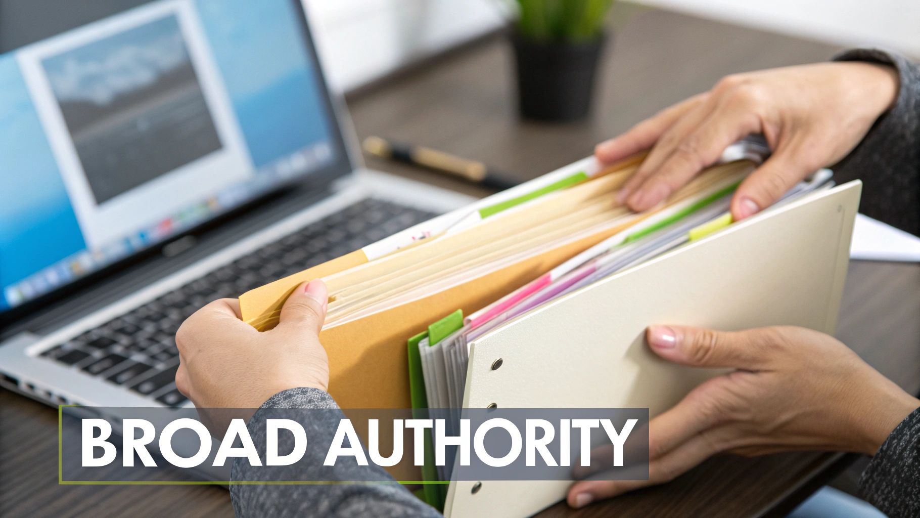 Hands sorting through files in folders on a desk with an open laptop, showing organization.