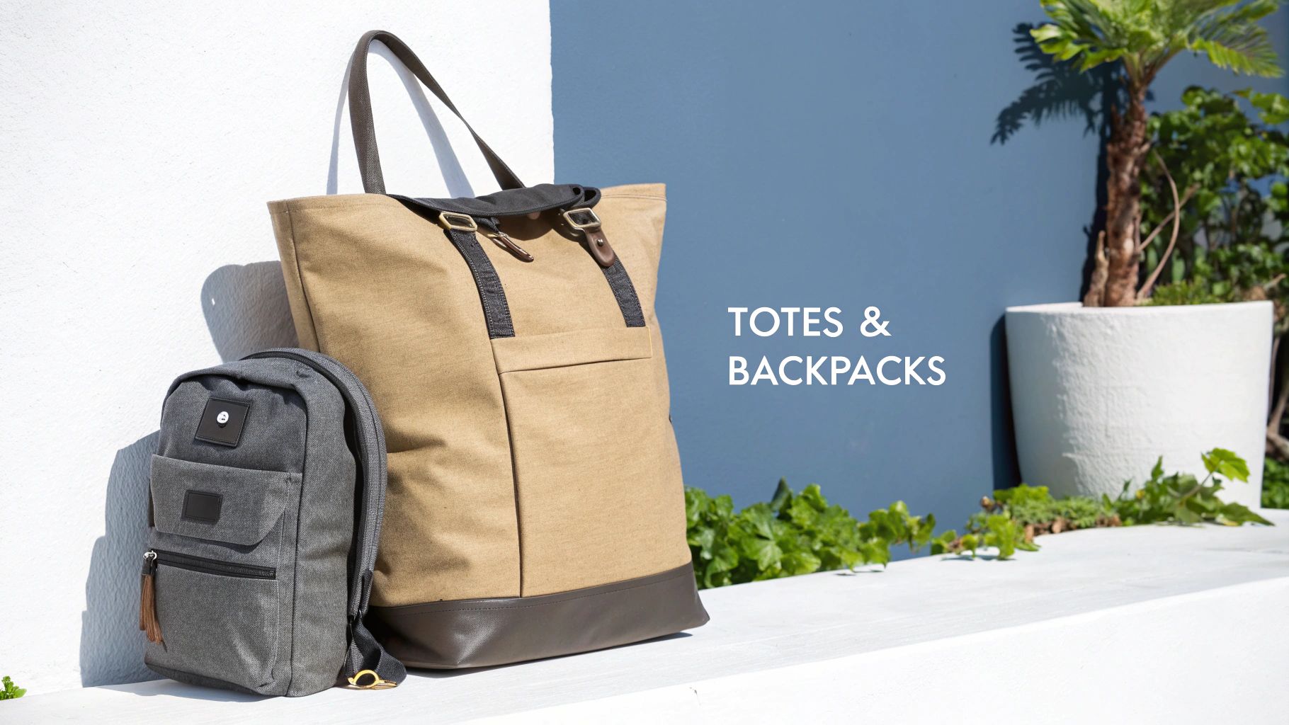 A large tan tote bag and a grey backpack leaning against a white wall with blue background and green plants.