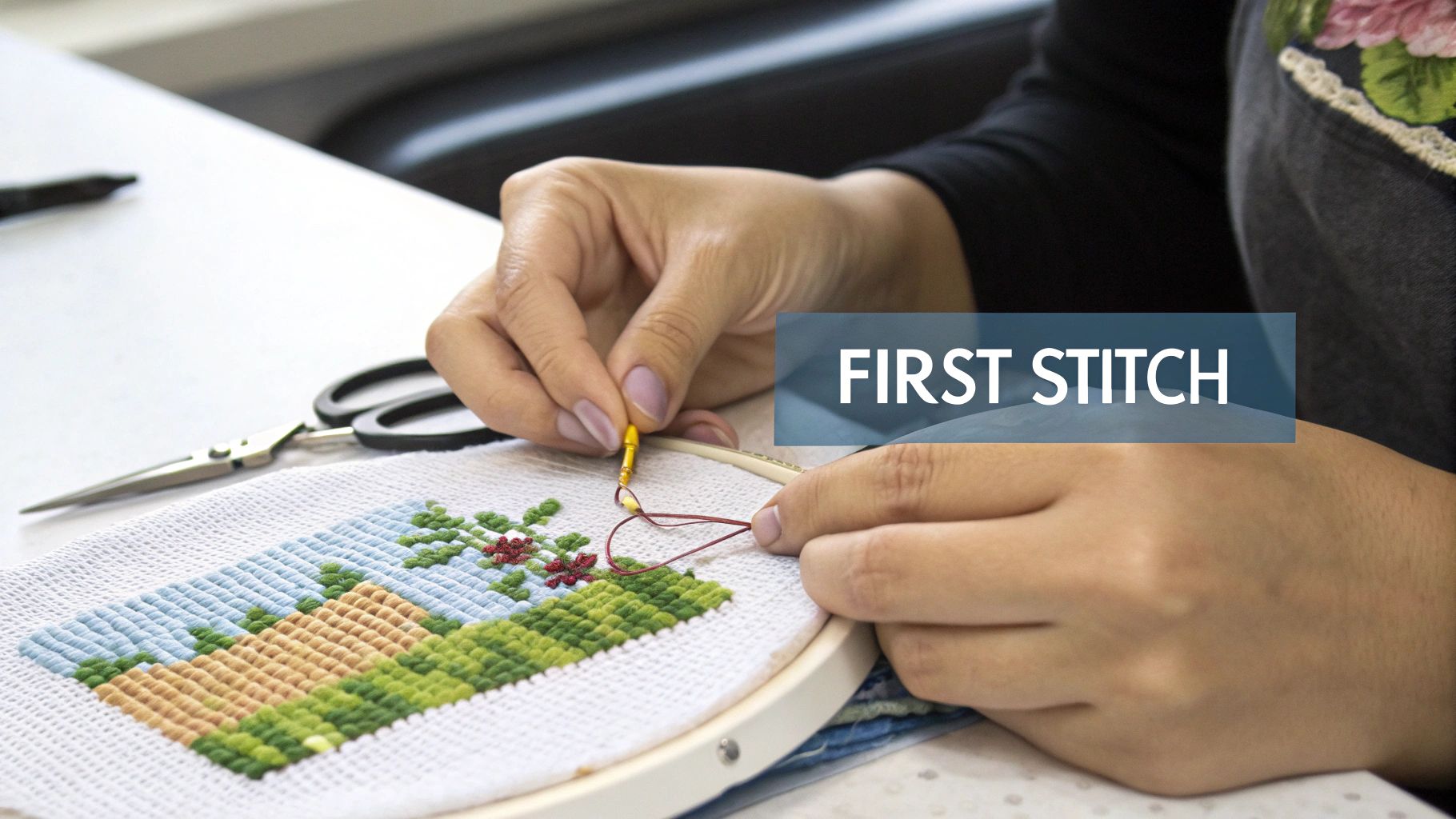Close-up of hands doing cross-stitch embroidery with colorful threads, creating a landscape design in a hoop.