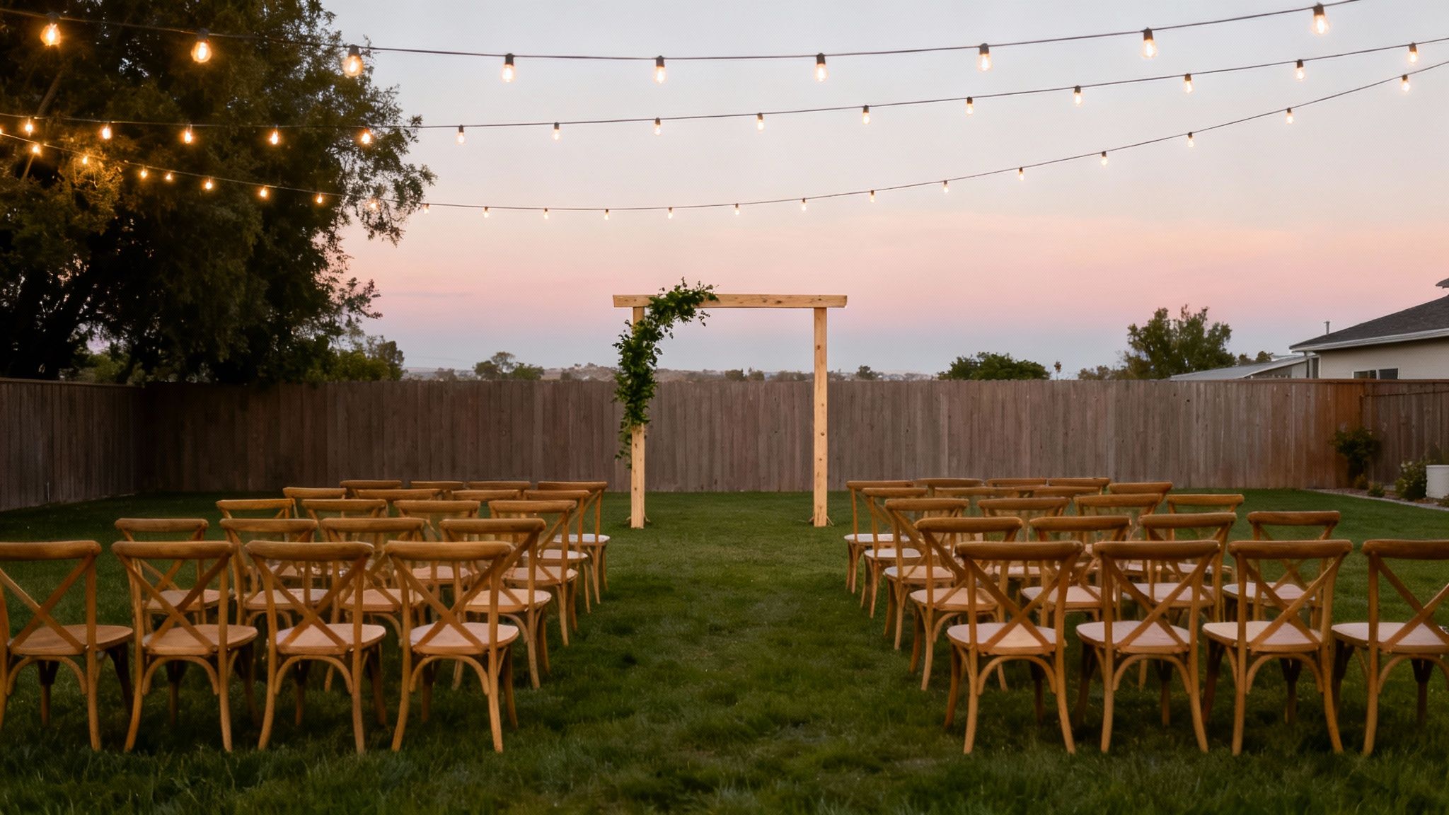 An outdoor wedding ceremony setup with rows of chairs, a decorated arch, and string lights.