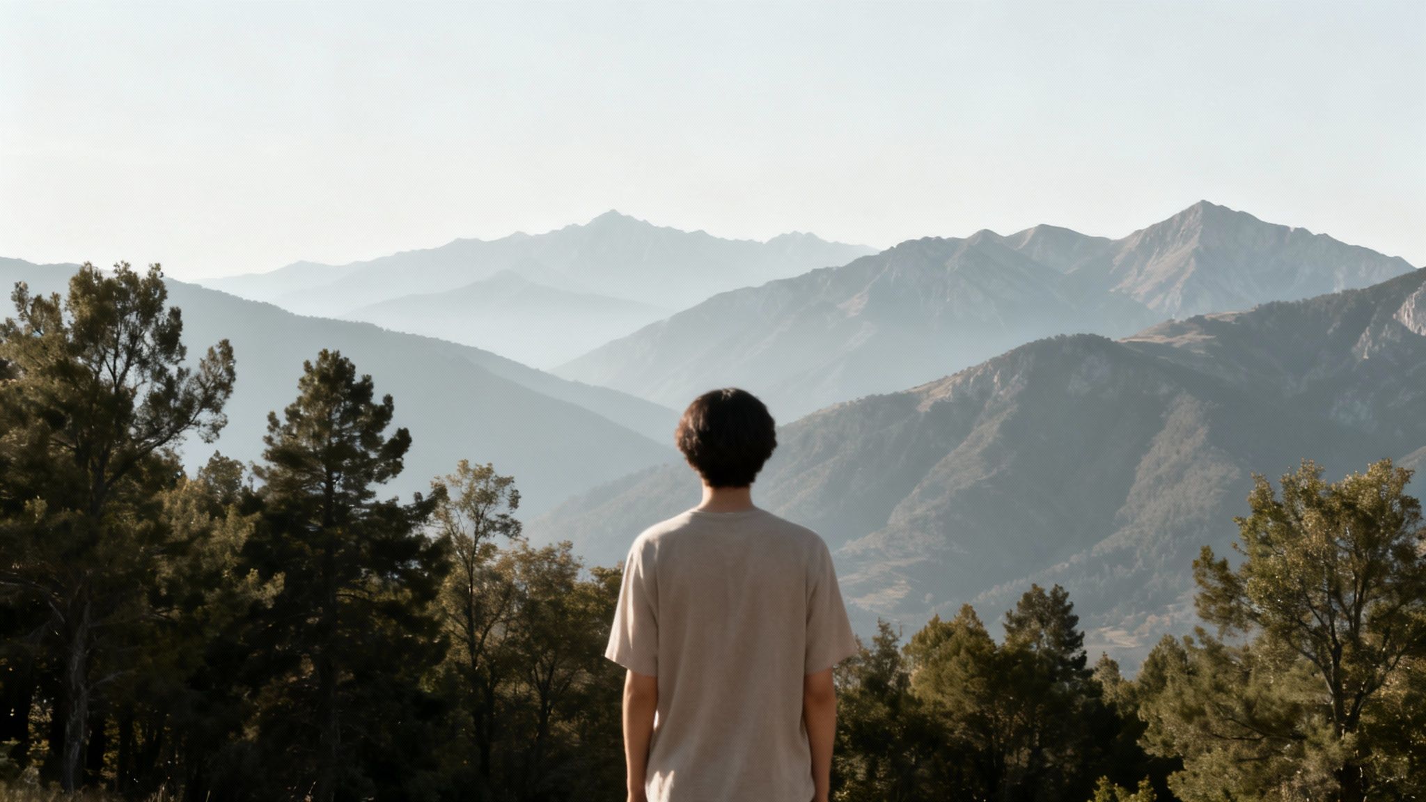 A person stands with their back to the camera, overlooking a layered mountain landscape.