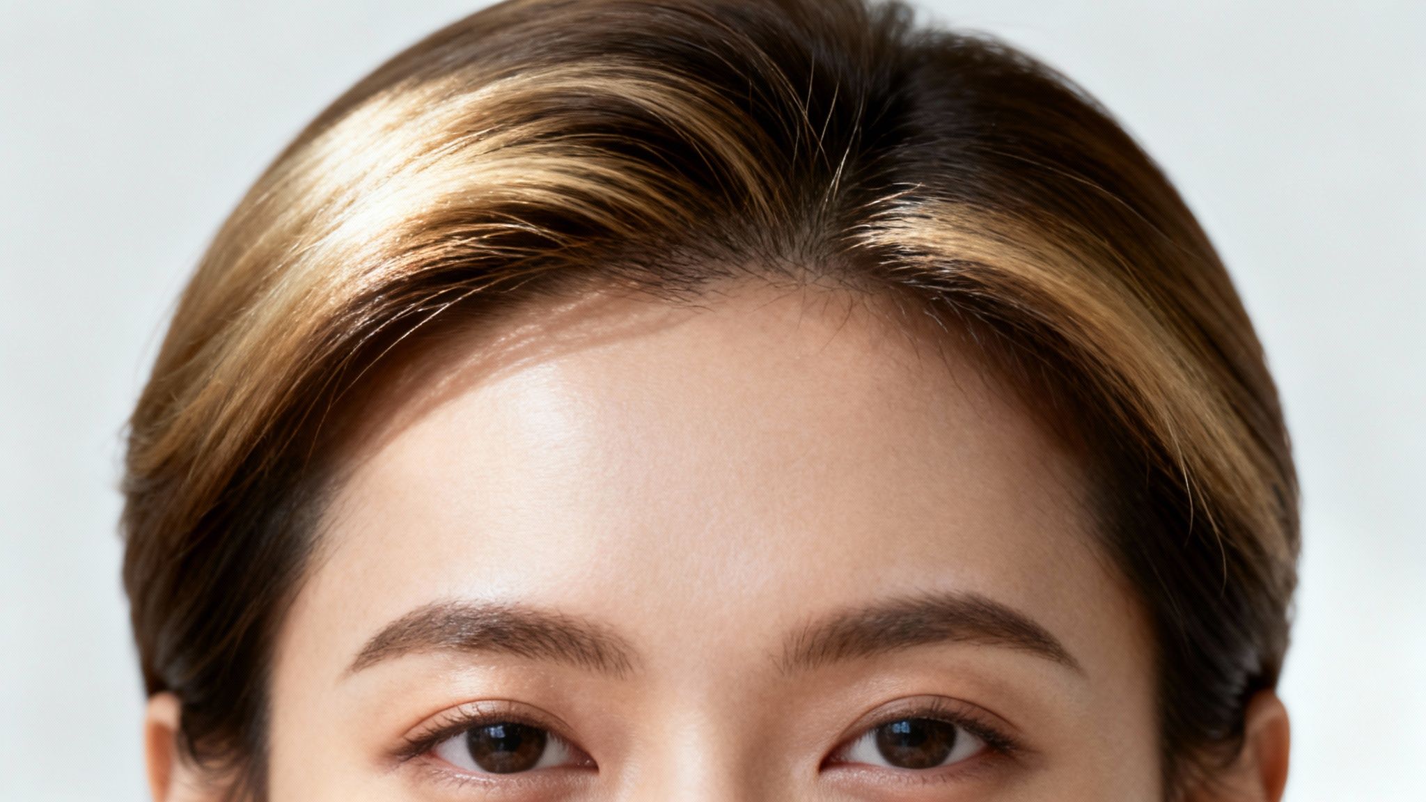 Close-up of an Asian woman's eyes, eyebrows, forehead, and highlighted brown hair.