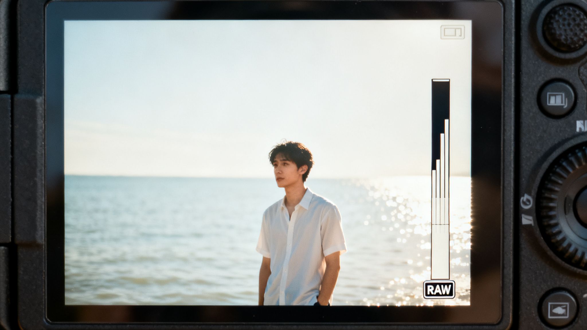 Close-up of a digital camera screen displaying a young man on a sunny beach.