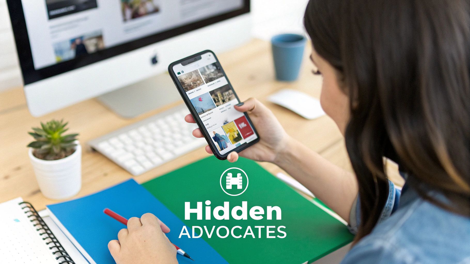 A person uses a smartphone with an app displaying images while taking notes at a modern desk.