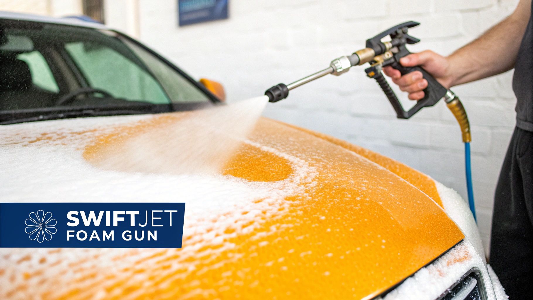 A person uses a Swiftjet foam gun to cover the orange hood of a car with white soap foam.