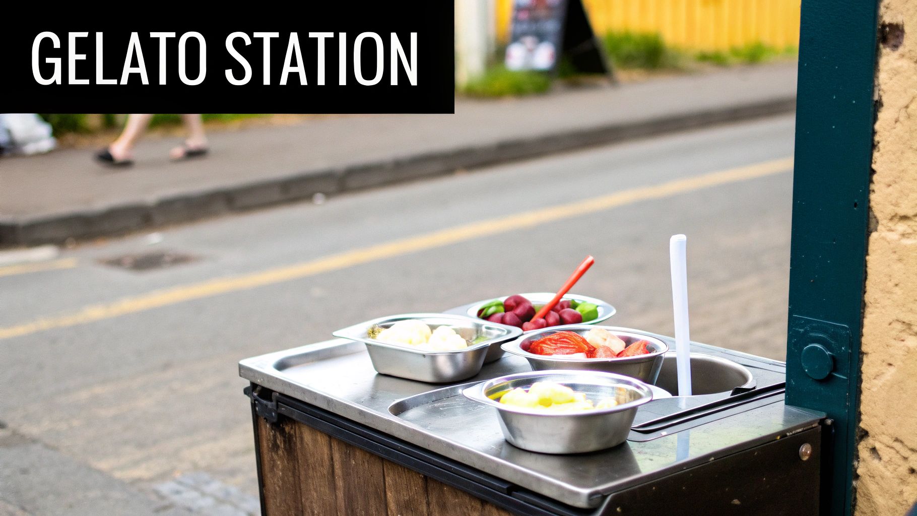 A street food stand labeled 'GELATO STATION' with multiple metal bowls of fruit toppings.