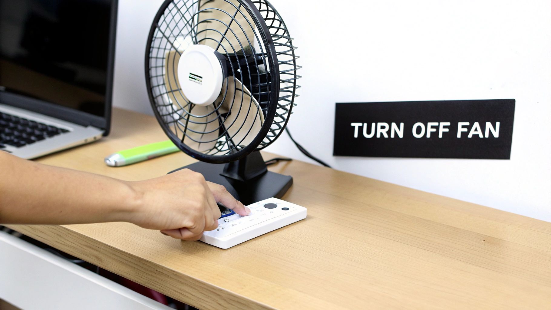 Hand pressing button on white remote control to turn off black desk fan