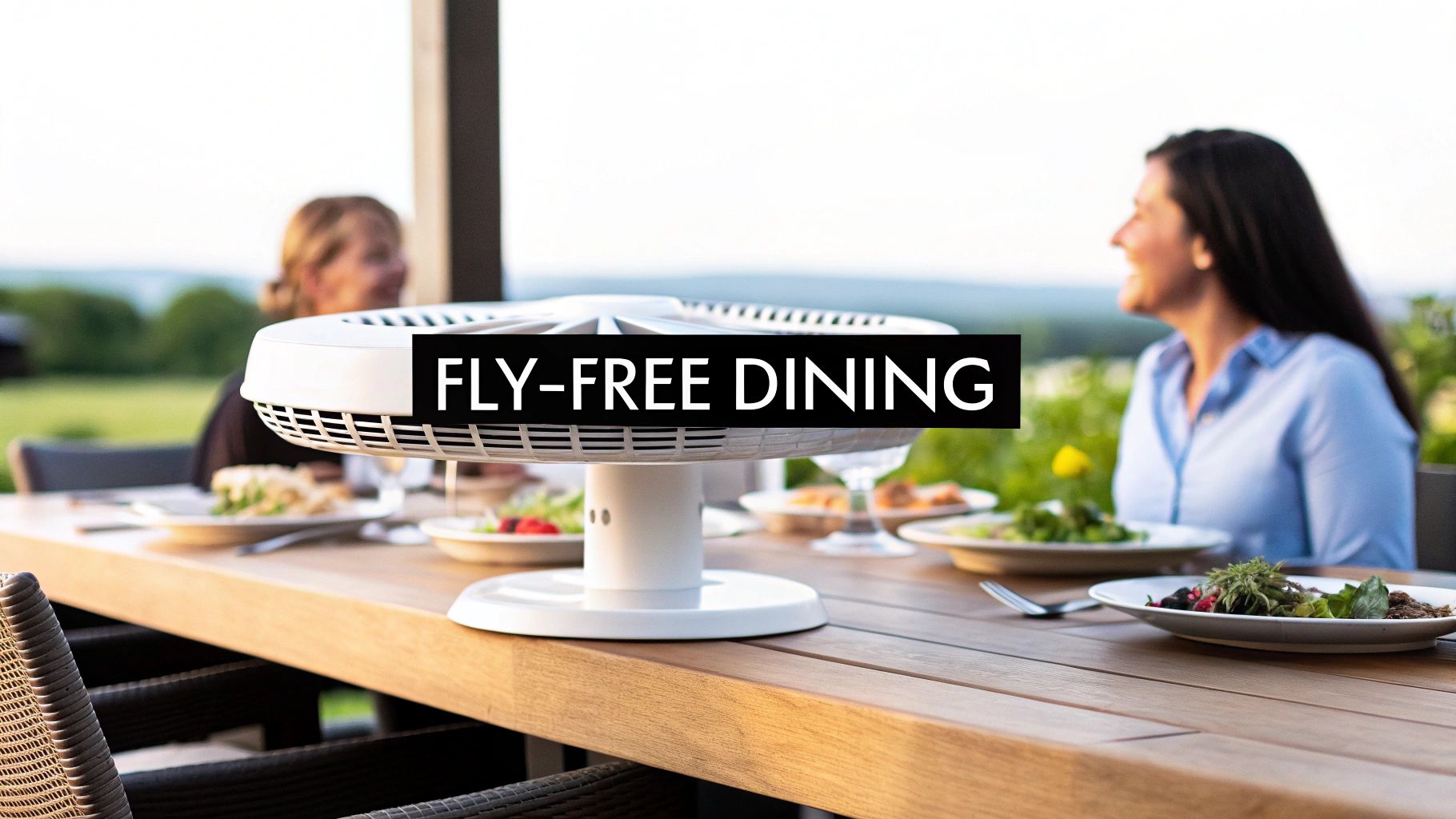 Two women enjoying an outdoor, fly-free dining experience with a white insect repellent device on a wooden table.