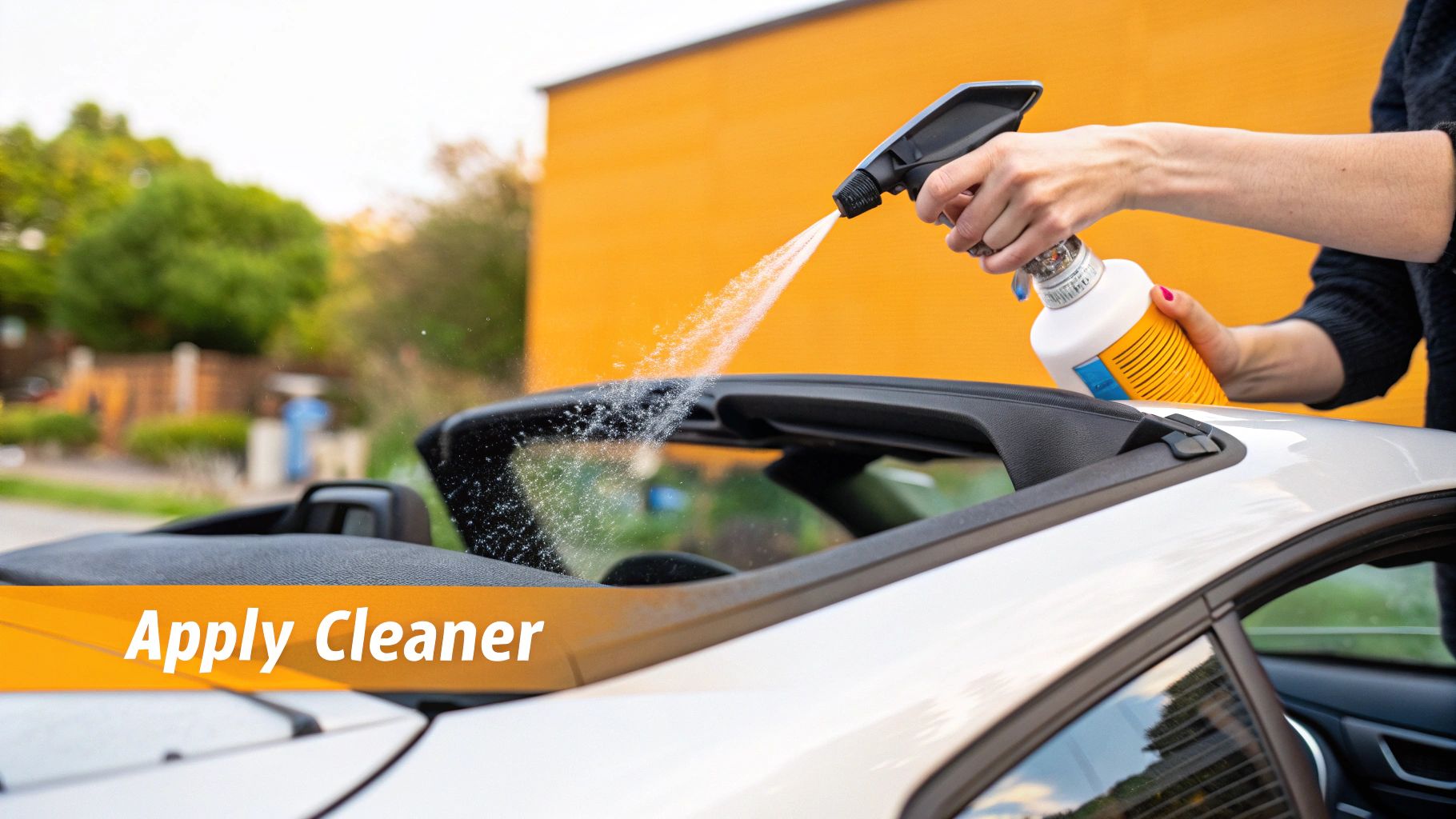 A person spraying a protectant solution evenly over a clean, dry black convertible top.