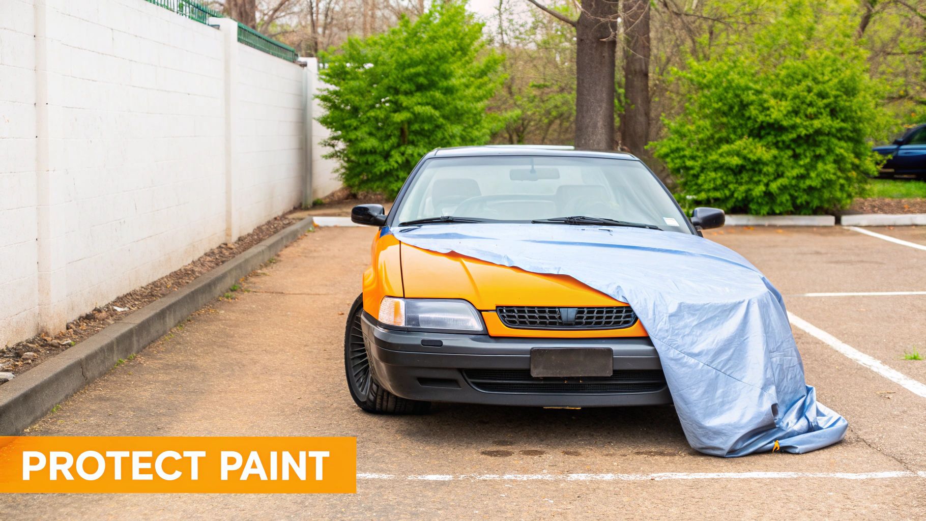 An orange car partially covered by a blue car cover is parked outdoors, protecting its paint.