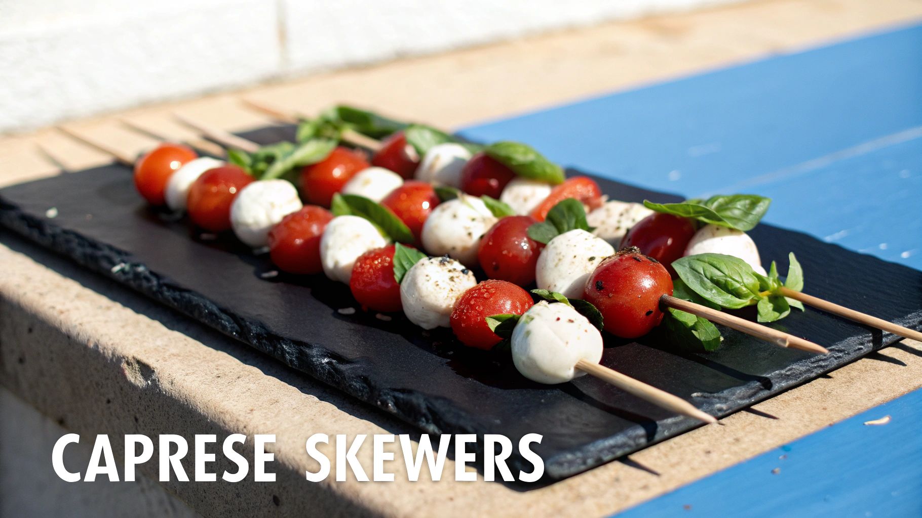 Caprese skewers featuring cherry tomatoes, fresh mozzarella balls, and basil leaves on a black slate board.