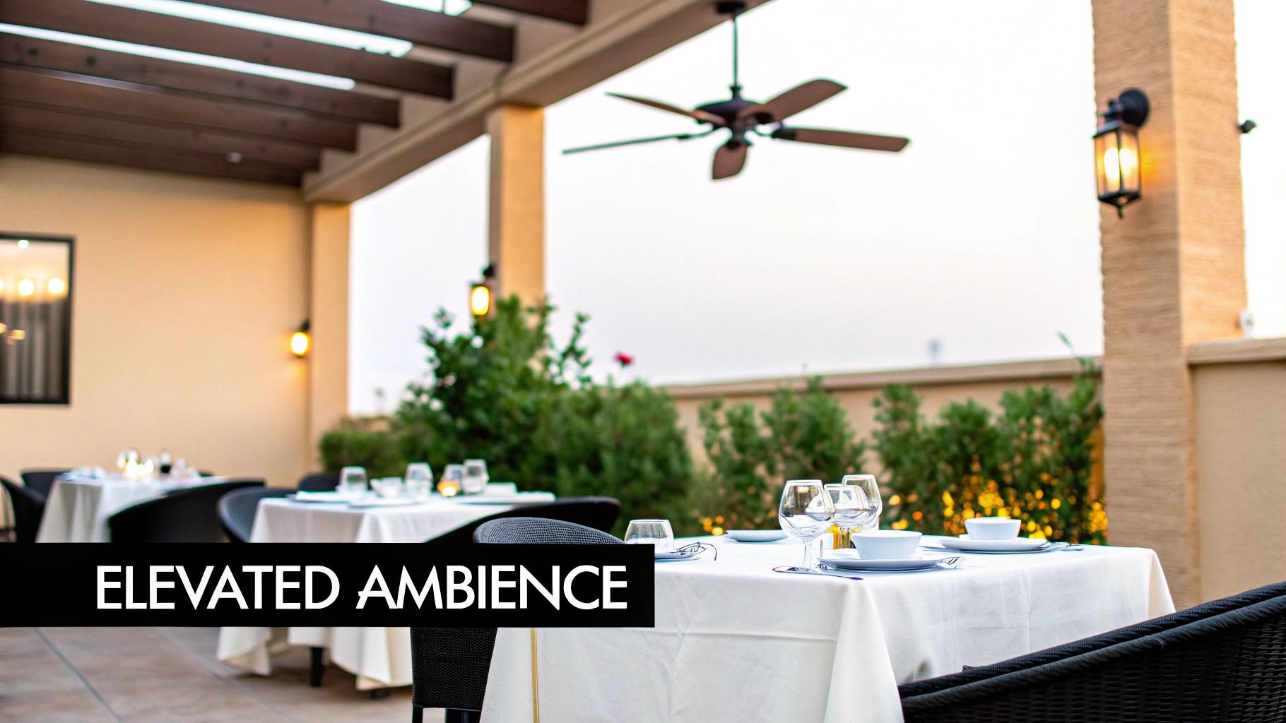 Elegant outdoor dining patio with set tables, ceiling fan, and warm lighting, creating an inviting ambiance.