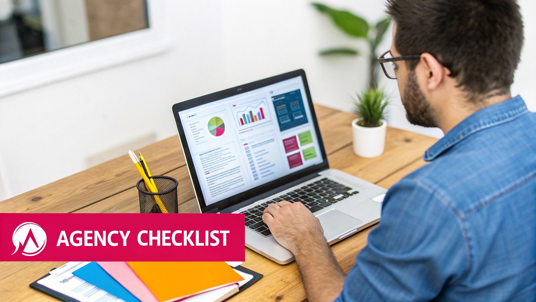 A man in a denim shirt and glasses works on a laptop displaying data analytics charts and graphs.