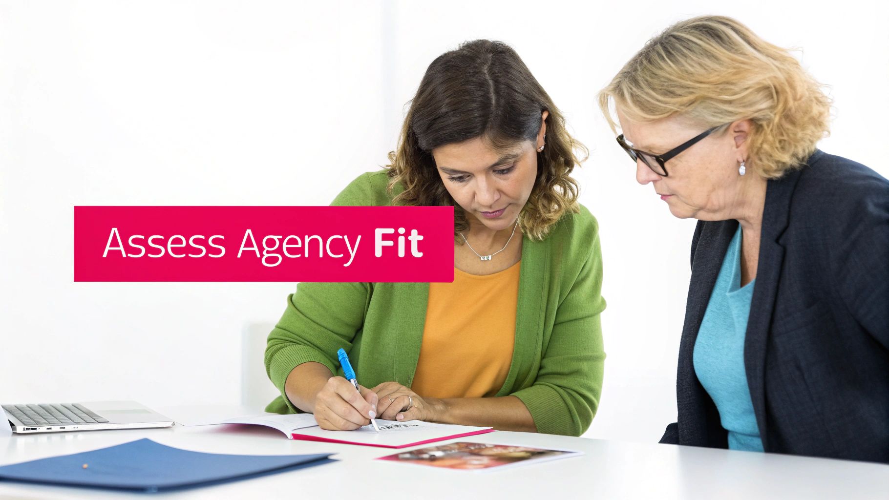 Two professional women collaborating on agency assessment documents at modern office workspace