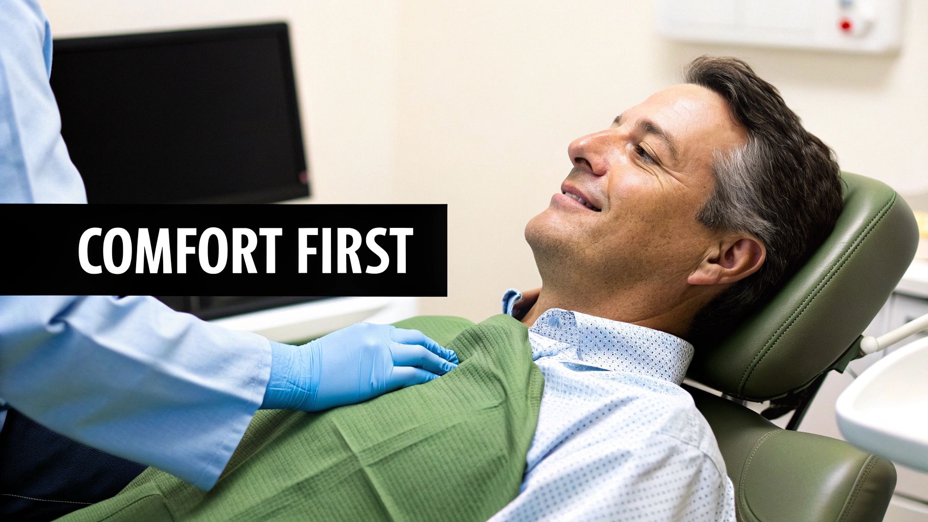 A smiling man comfortably reclined in a dental chair with a dentist's gloved hand, emphasizing comfort.