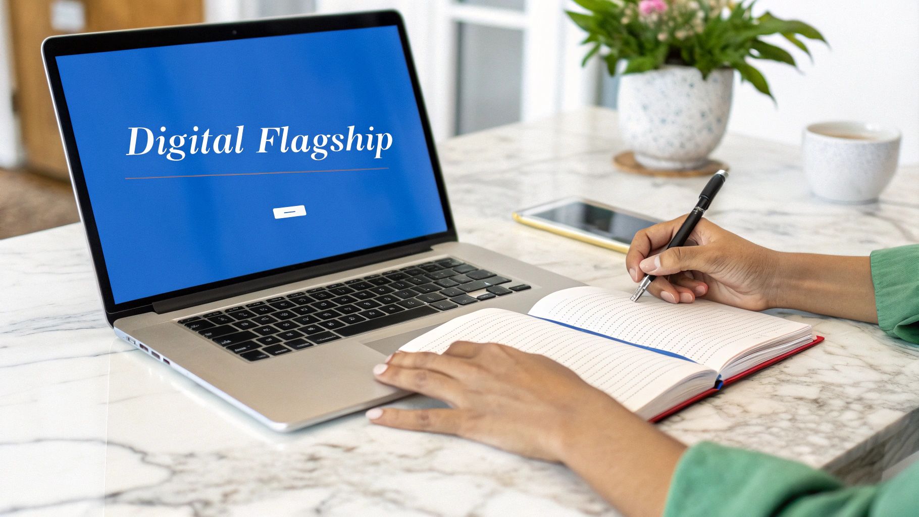 A person writes in a notebook with a pen next to a laptop displaying 'Digital Flagship' on a blue screen.