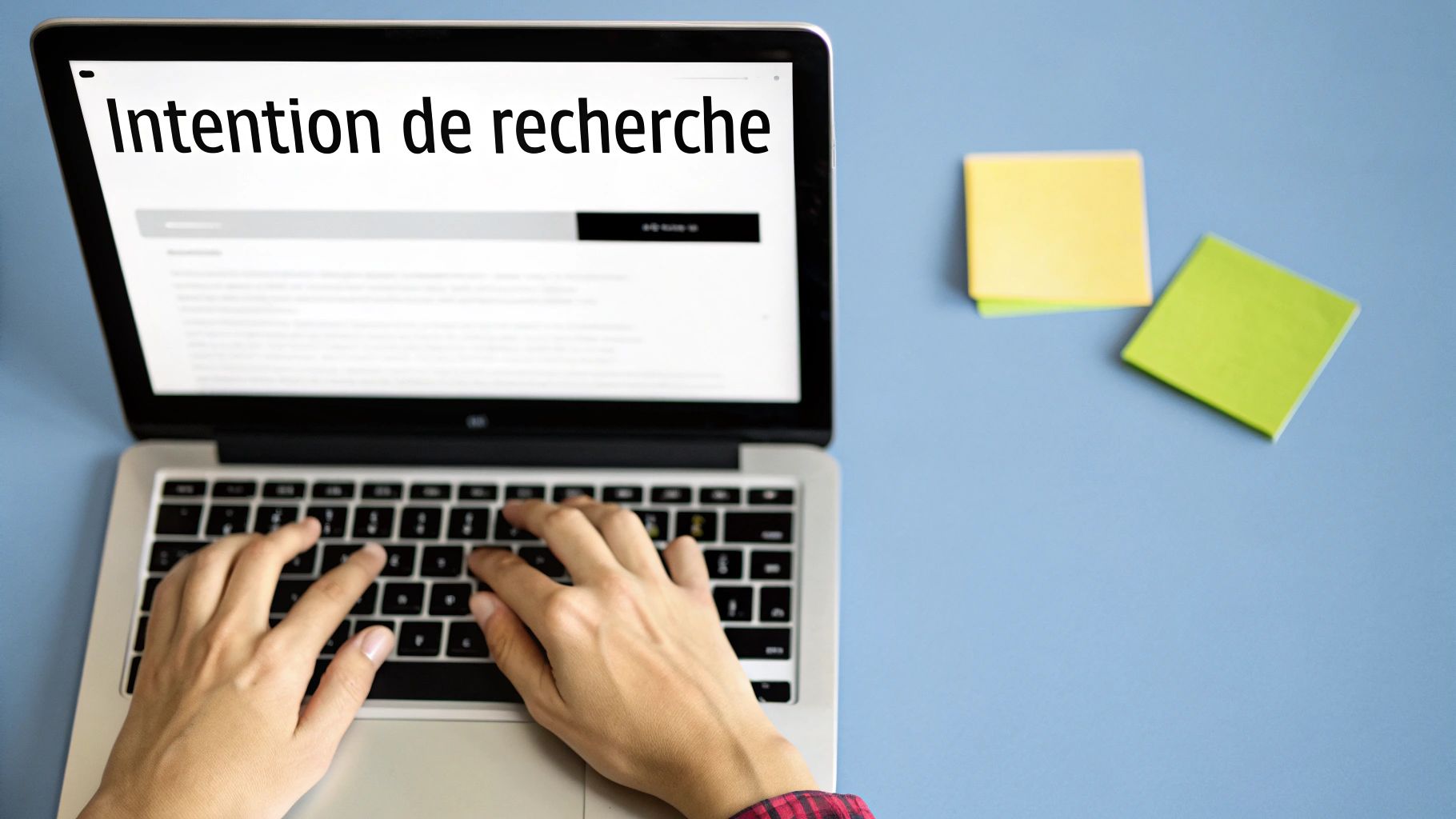 Une personne tape sur un ordinateur portable affichant "Intention de recherche", avec des post-it à côté.