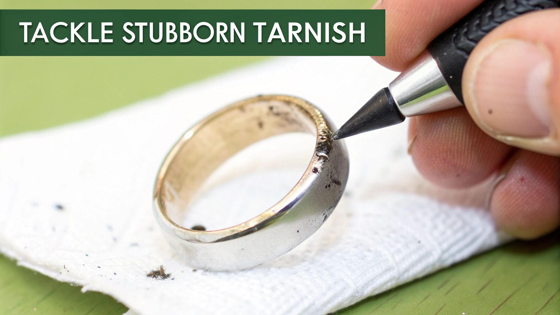 A hand uses a specialized tool to meticulously remove stubborn tarnish from a silver ring resting on a white cloth.