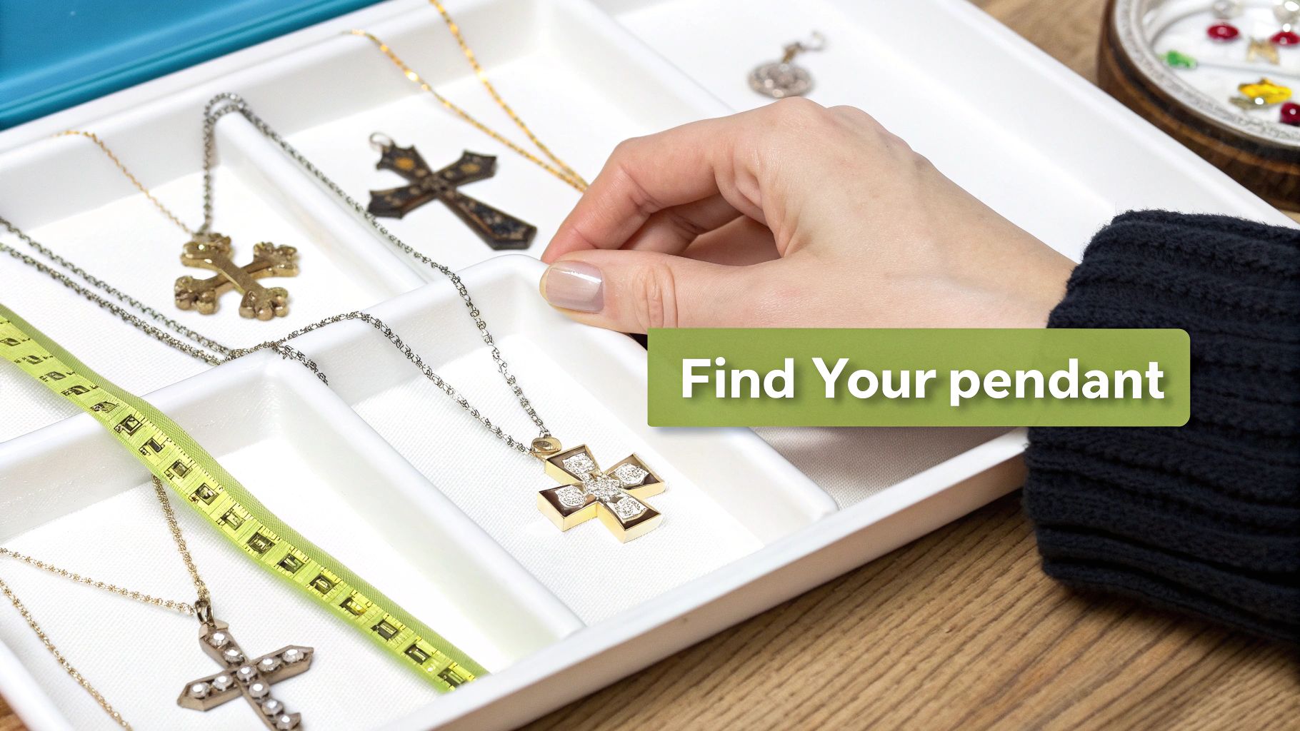 A hand selects a diamond-studded gold cross pendant from a white jewelry box, surrounded by other cross necklaces and a measuring tape.