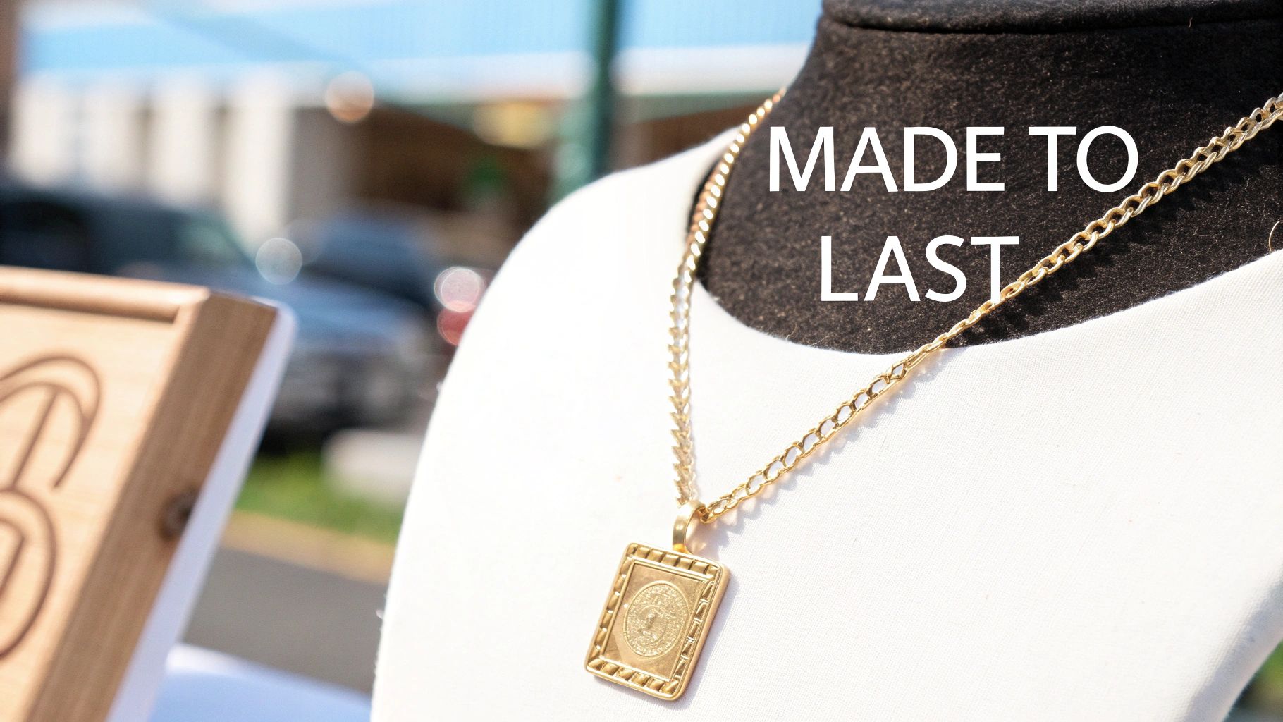 A gold rectangular pendant necklace with an intricate design displayed on a white mannequin bust, with 'MADE TO LAST' text.