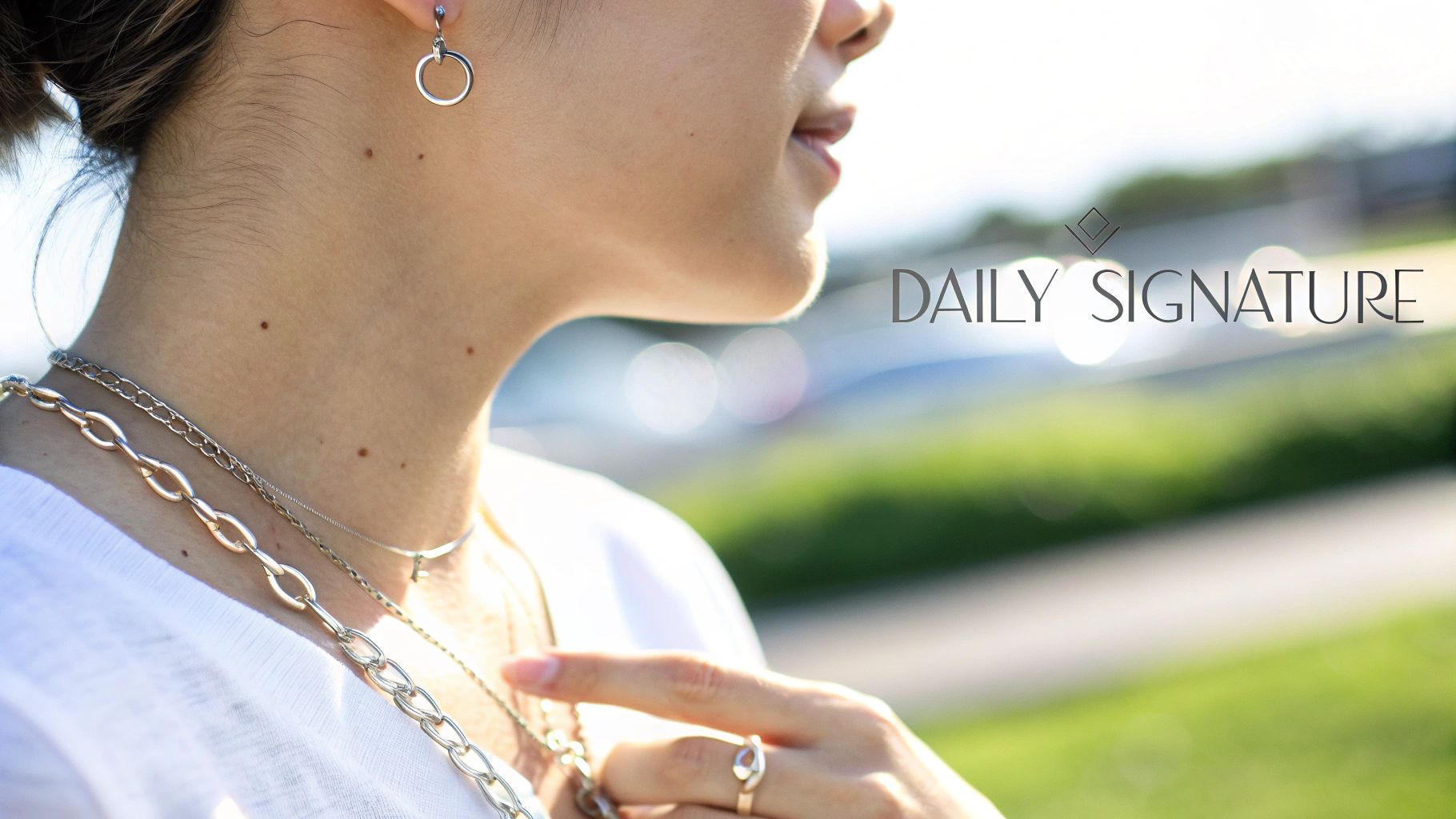Close-up of a woman wearing silver hoop earrings, layered chain necklaces, and a stylish ring.